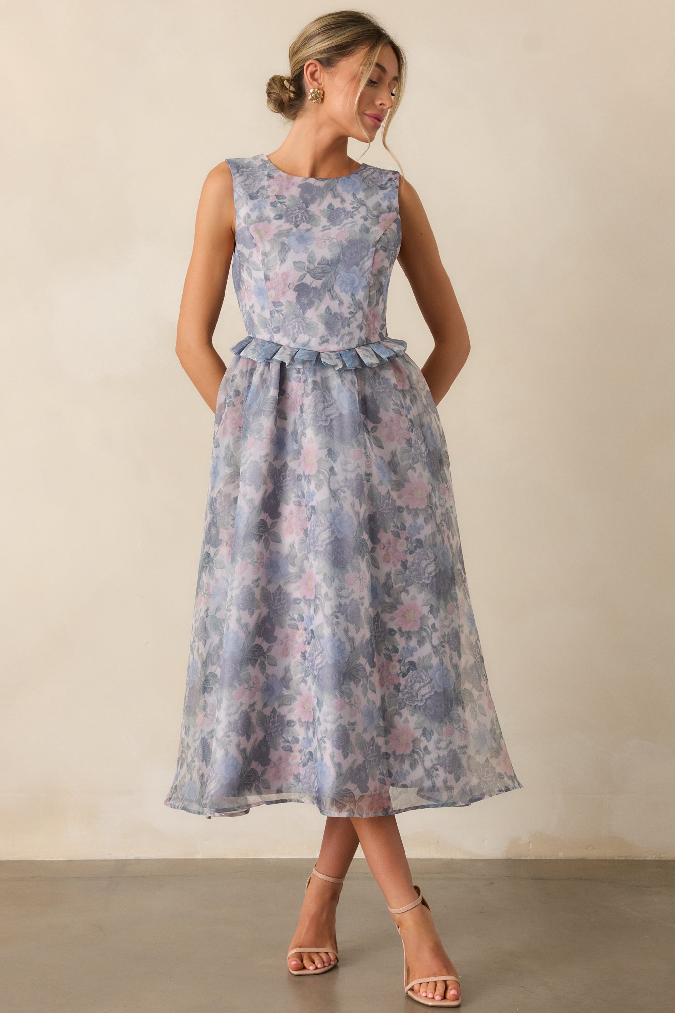 A full-body image highlighting the ash blue floral dress with a rounded neckline, floral design, ruffled peplum waistband, and a relaxed midi skirt, creating a flattering and comfortable silhouette.