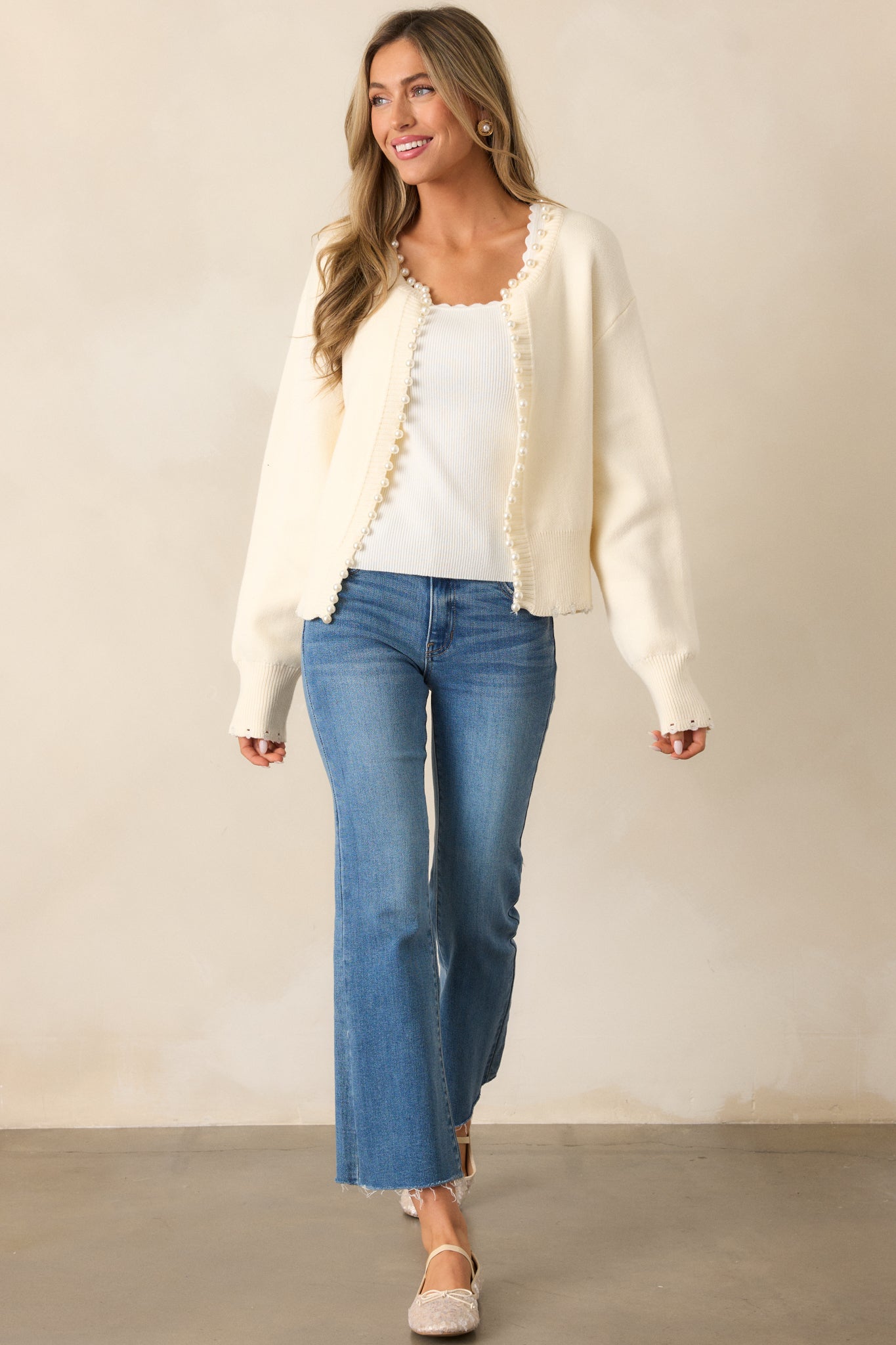 An ivory cardigan with a rounded neckline, a faux pearl rim, and long sleeves. The rib knit cuffs complete its polished look.