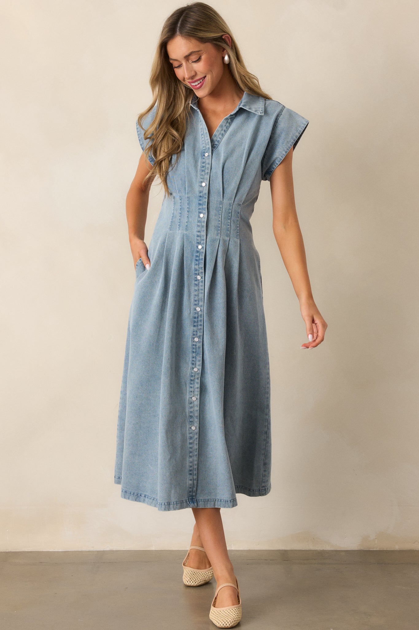 Full view of the light wash dress highlighting its cap sleeves, pearlized button closures, and pleated waist detail.