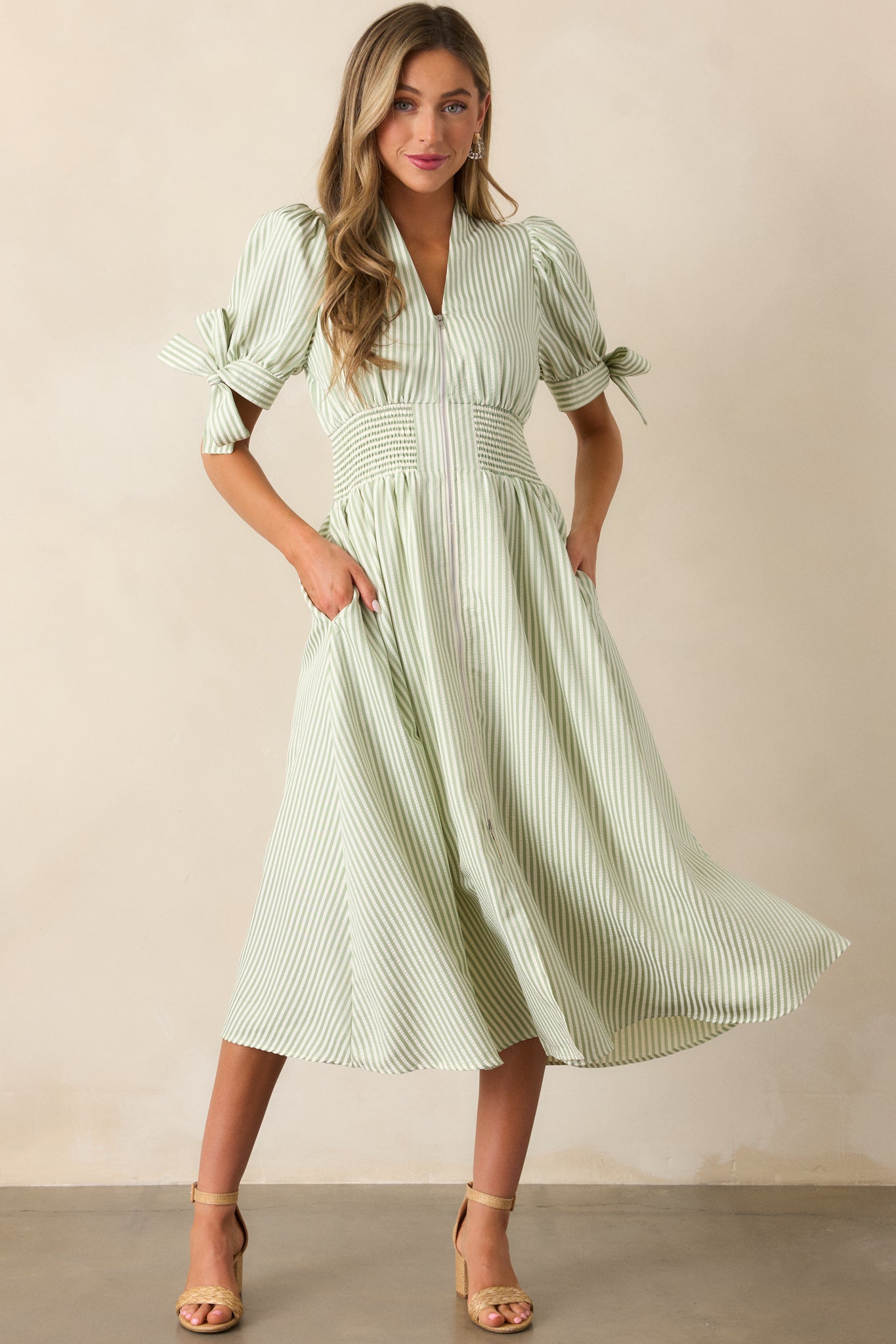 Green stripe dress showcasing a smocked waist, V-neck neckline, and front zipper, complemented by tie accents at the sleeve cuffs and a flowing skirt.