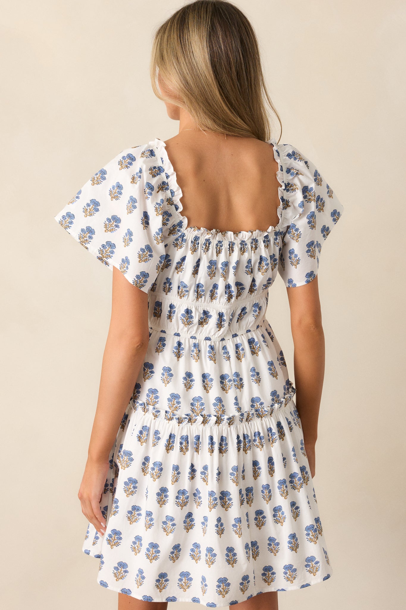 Back view of the ivory dress, showcasing the blue floral pattern and the placement of the decorative ribbon ties along the bodice tiers.