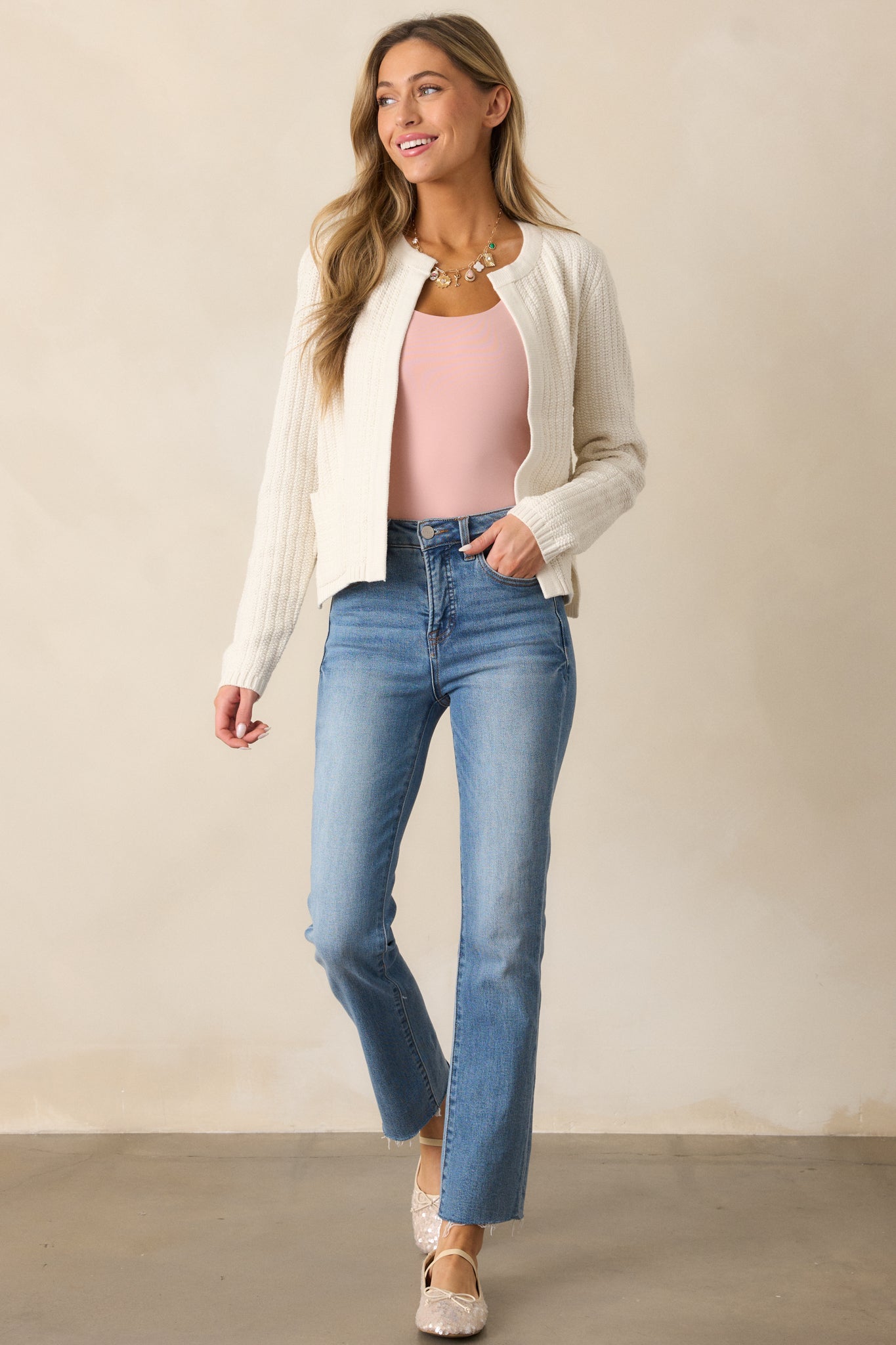 A full view of the ivory cardigan, highlighting the relaxed fit, long sleeves, and functional pockets in its knit design.