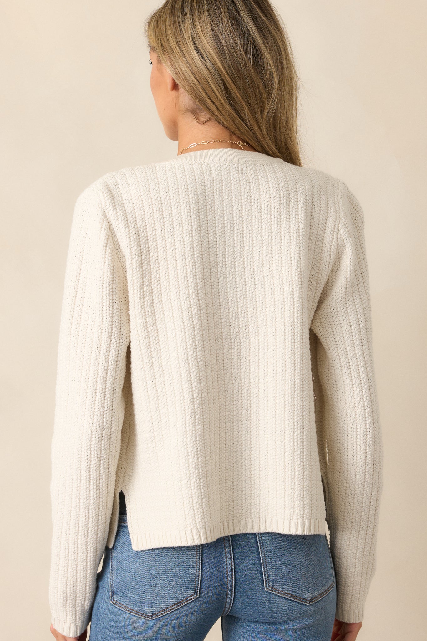 A view of the ivory cardigan from behind, showcasing the long sleeves and knit design.