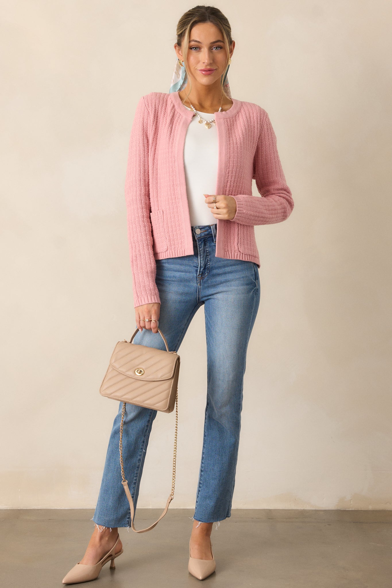 Full-length image of a rose cardigan featuring a knit texture, long sleeves, and a rounded neckline, styled with the pockets slightly in use.