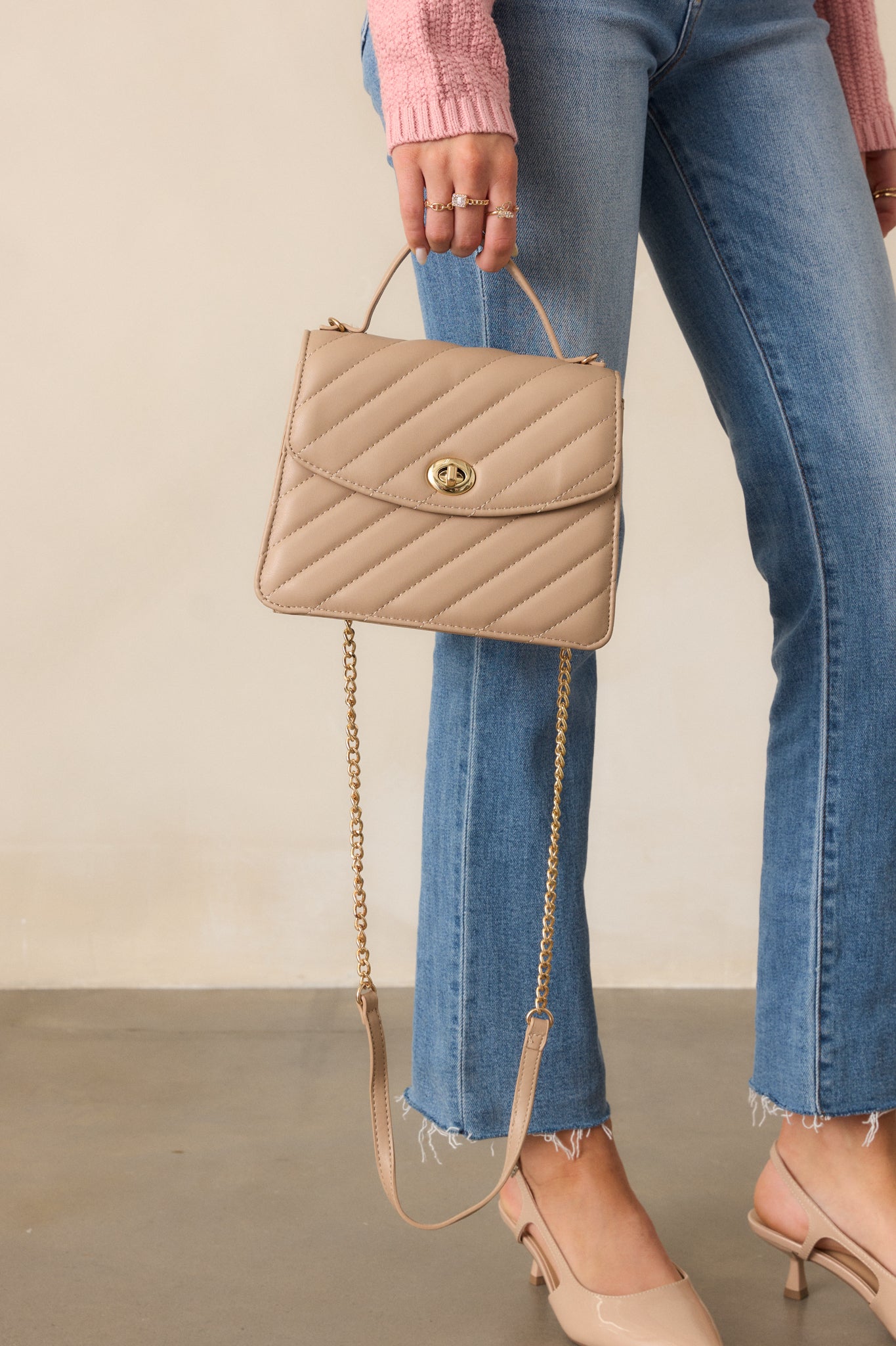 A front view of the light mocha handbag, highlighting the quilted texture, the thin solid handle, and the gold twist lock closure, with the optional shoulder strap draped on the side.