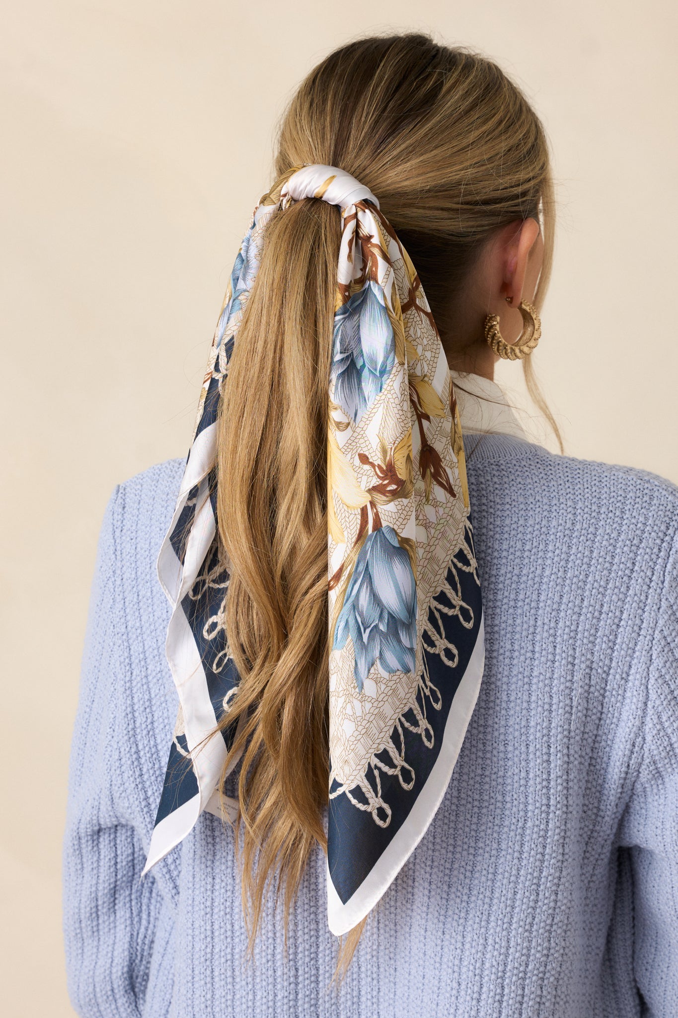 A navy satin scarf featuring a gold and blue floral design with a contrasting navy trim along the edges.