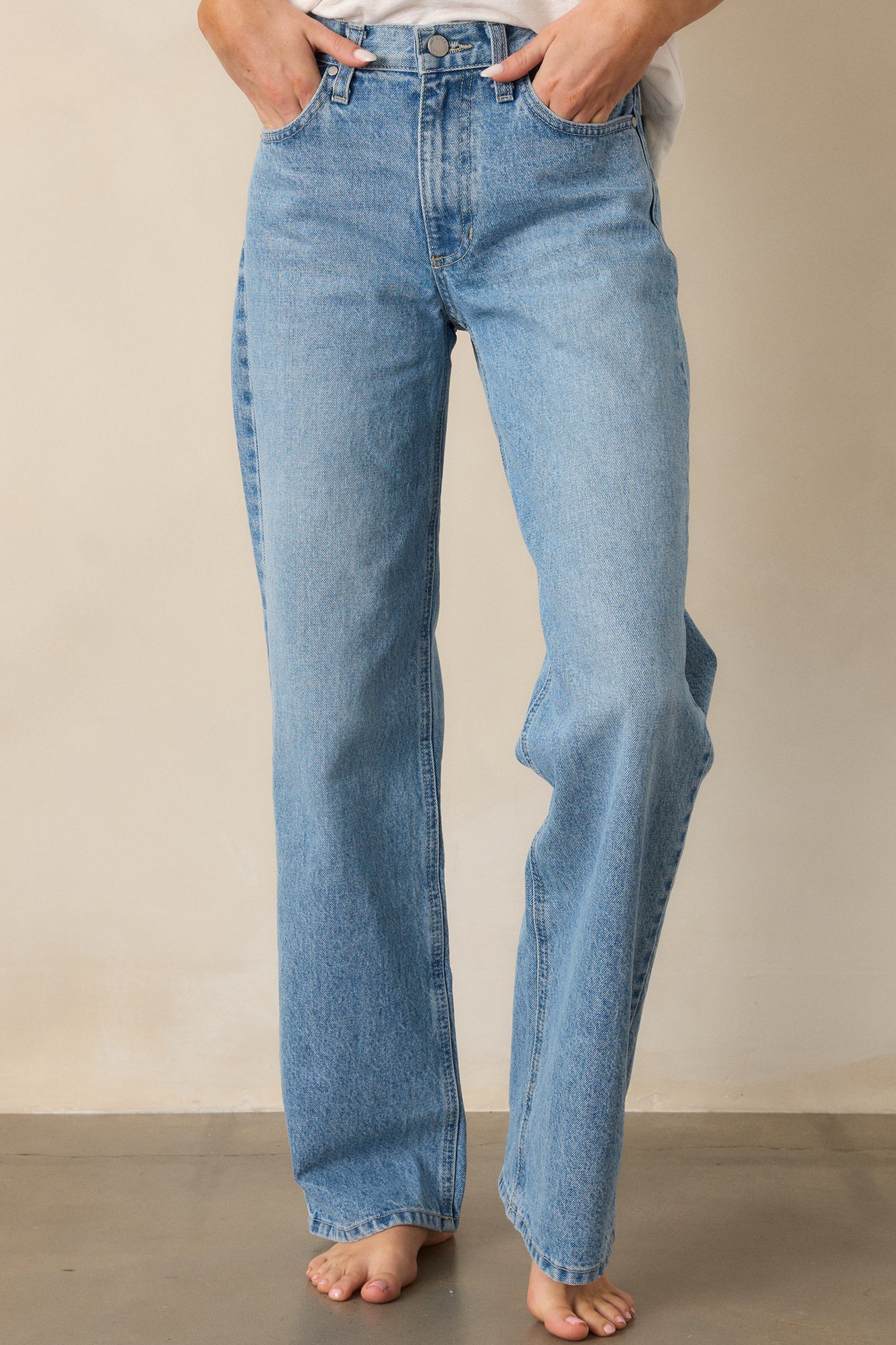 A close-up of the light wash jeans, highlighting the relaxed fit and the straight leg cut, with a focus on the waist detailing and the button and zipper closure.