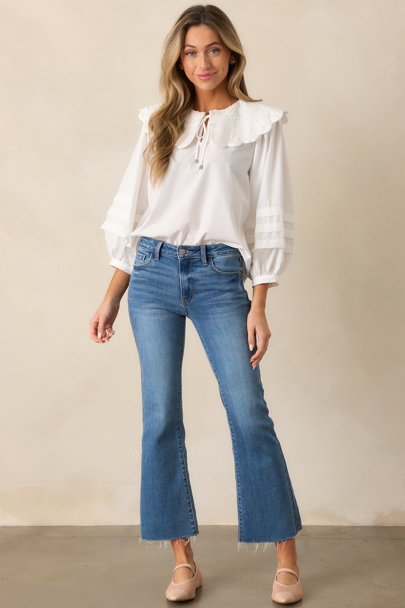 A full-length view of the ivory blouse, showcasing the large scalloped collar with floral embroidered detailing, the self-tie keyhole at the neckline, and the long puff sleeves with pleated details.