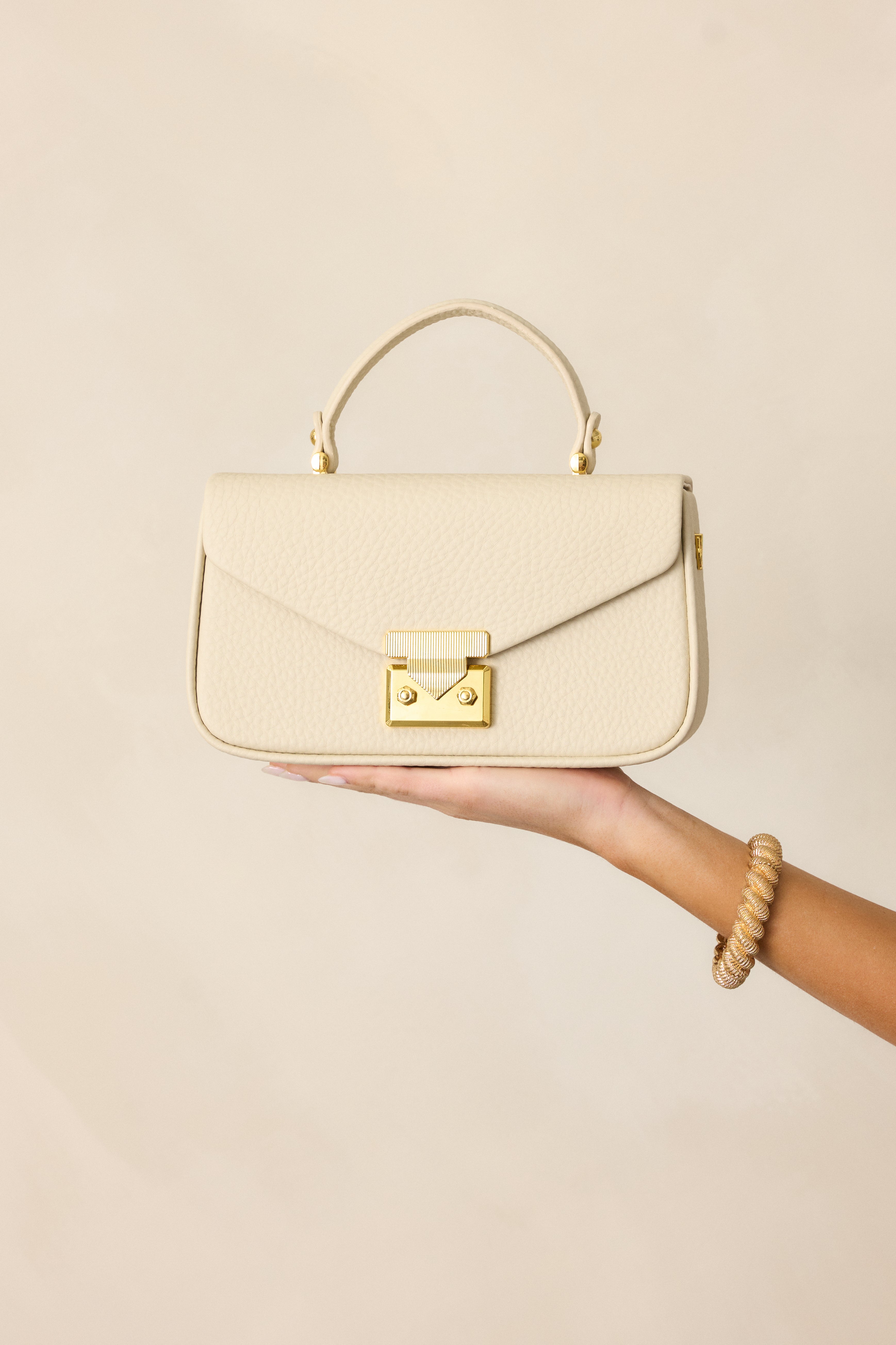 Cropped view of the ivory handbag highlighting the gold triangular clasp tuck lock and sleek faux leather texture.