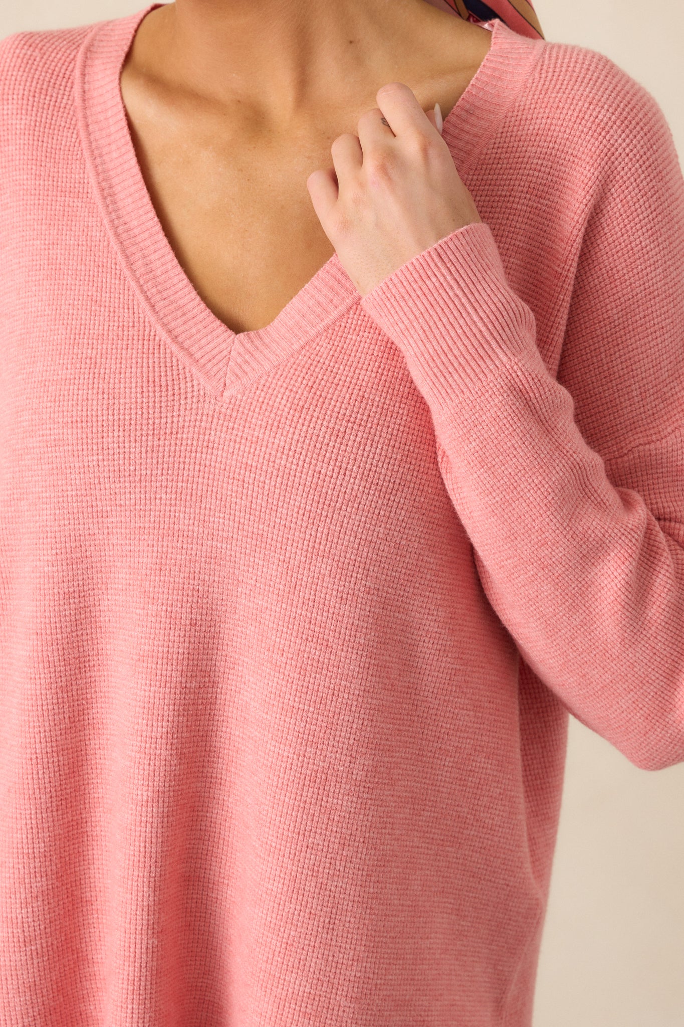 A close-up of the v-neckline and ribbed cuffs of the rose sweater, showcasing its soft knit texture and subtle design elements.