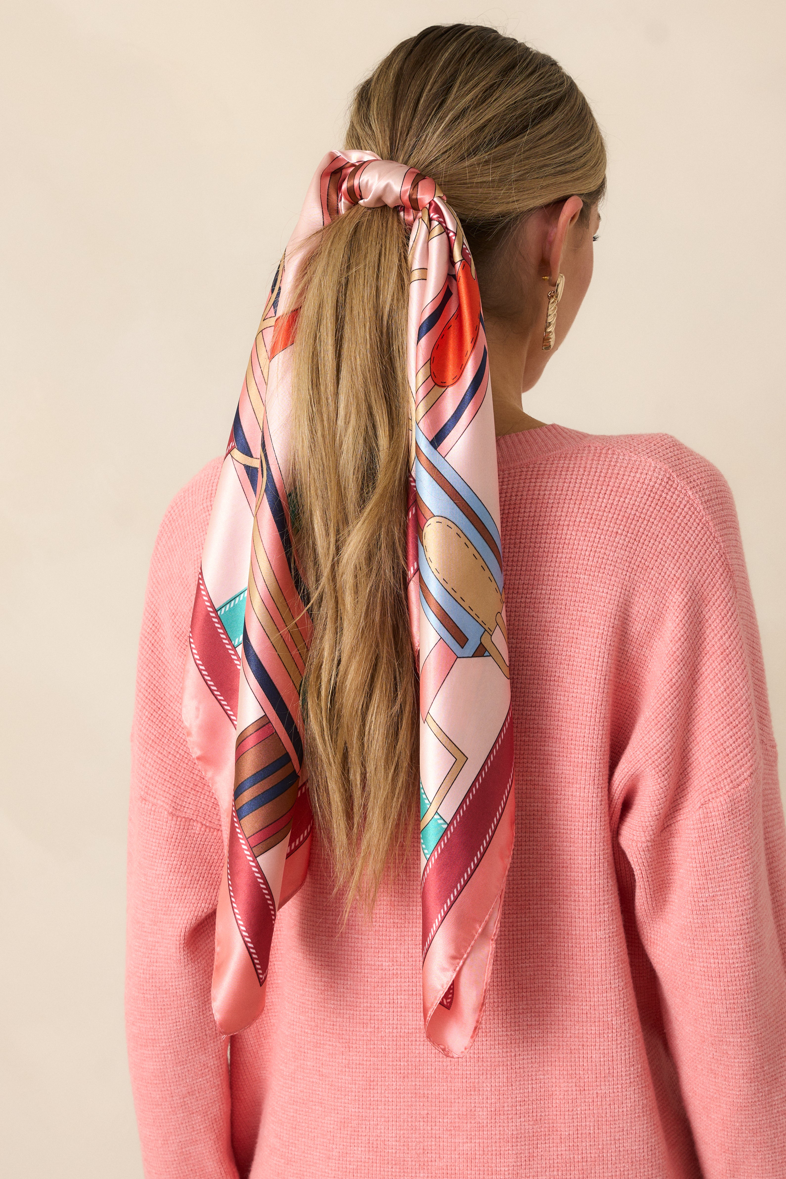 A pink satin scarf featuring a multicolored print, draped elegantly to showcase its vibrant, flowing design.