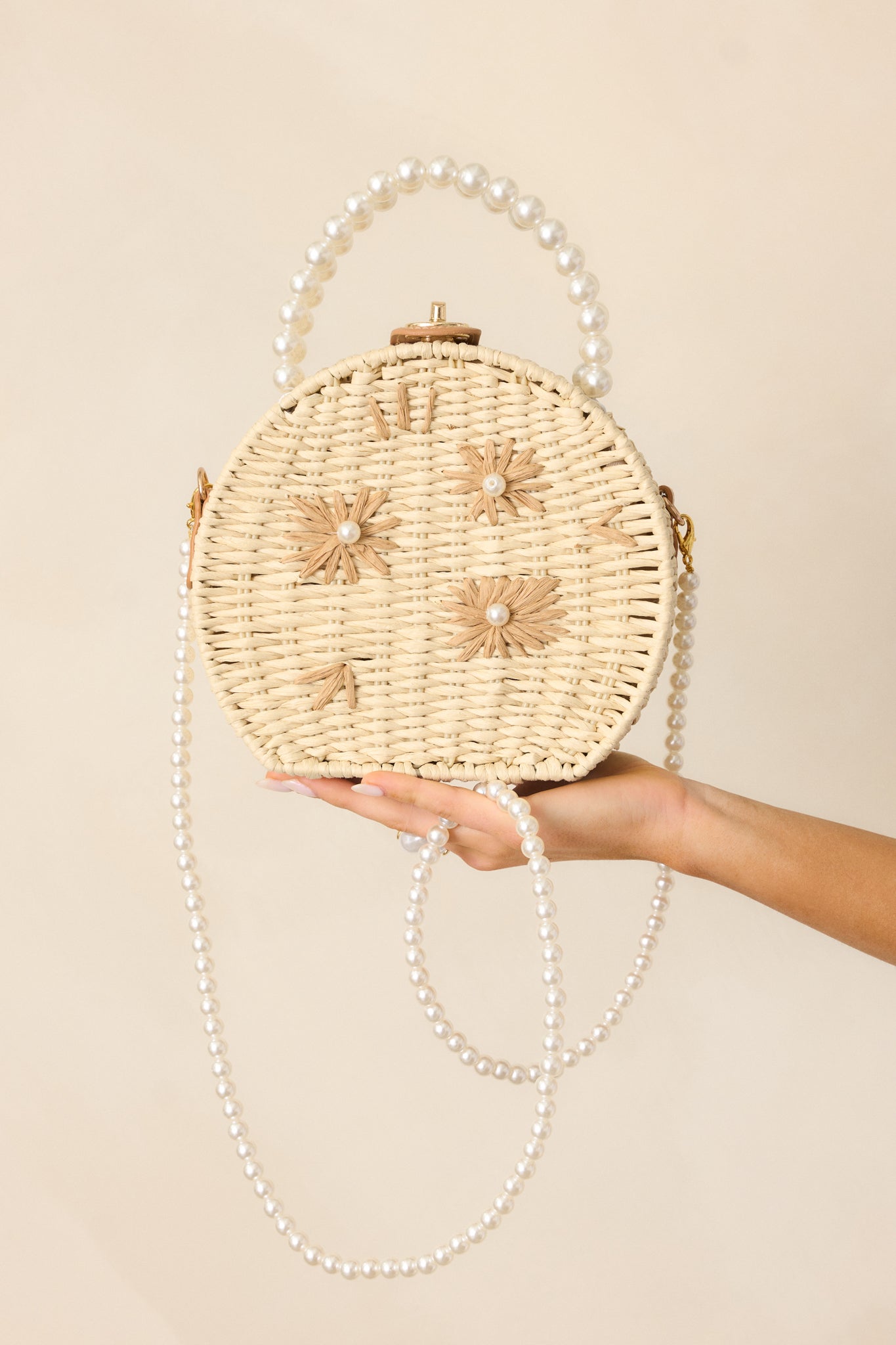  Ivory handbag in a circular shape, showcasing tan rattan flower accents with pearl centers, gold twist and lock closure, large faux ivory pearl beaded handles, and an optional faux pearl shoulder strap.