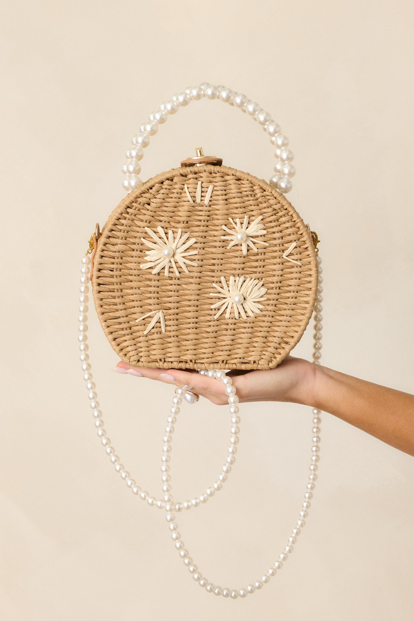 Cropped view of the tan handbag focusing on the circular design, small ivory rattan flower details, and gold twist and lock closure.