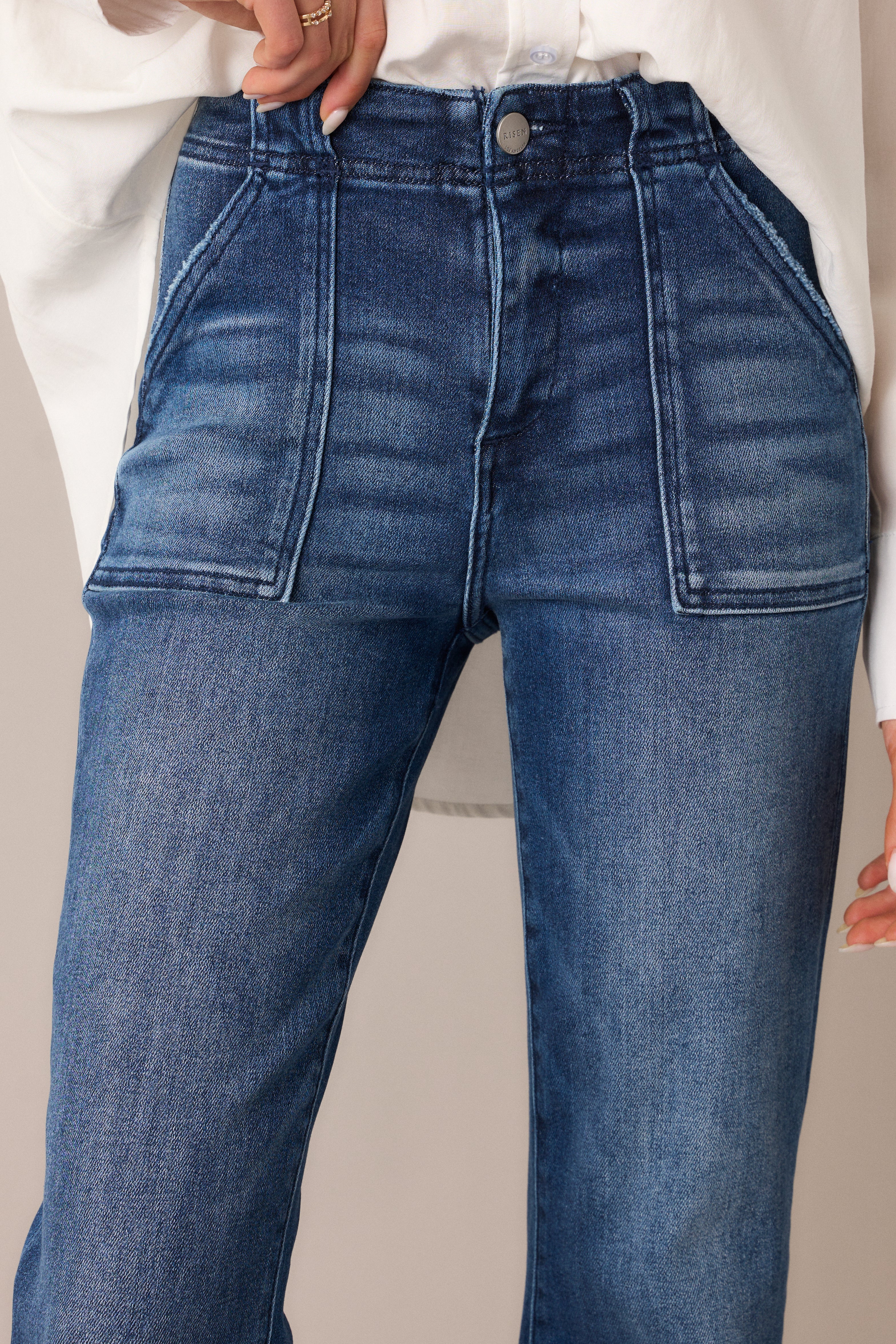  A focused view of the button and zipper closure, emphasizing the high waist design, large front pockets, and the dark, rich wash that gives these jeans their sharp, structured look.