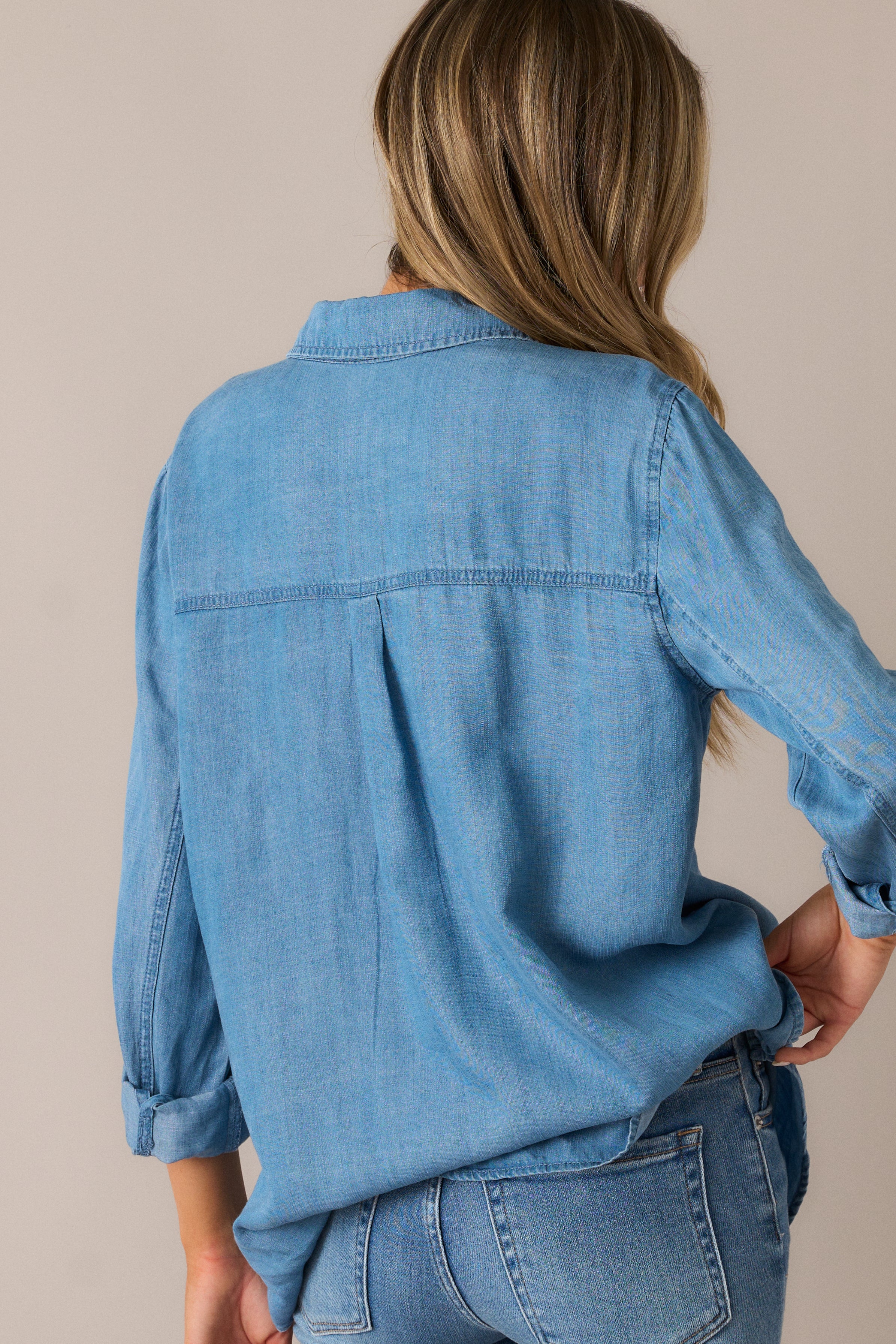 The chambray blouse from the back, showcasing its relaxed fit and curved split hem, offering a flattering, easygoing look from all angles.