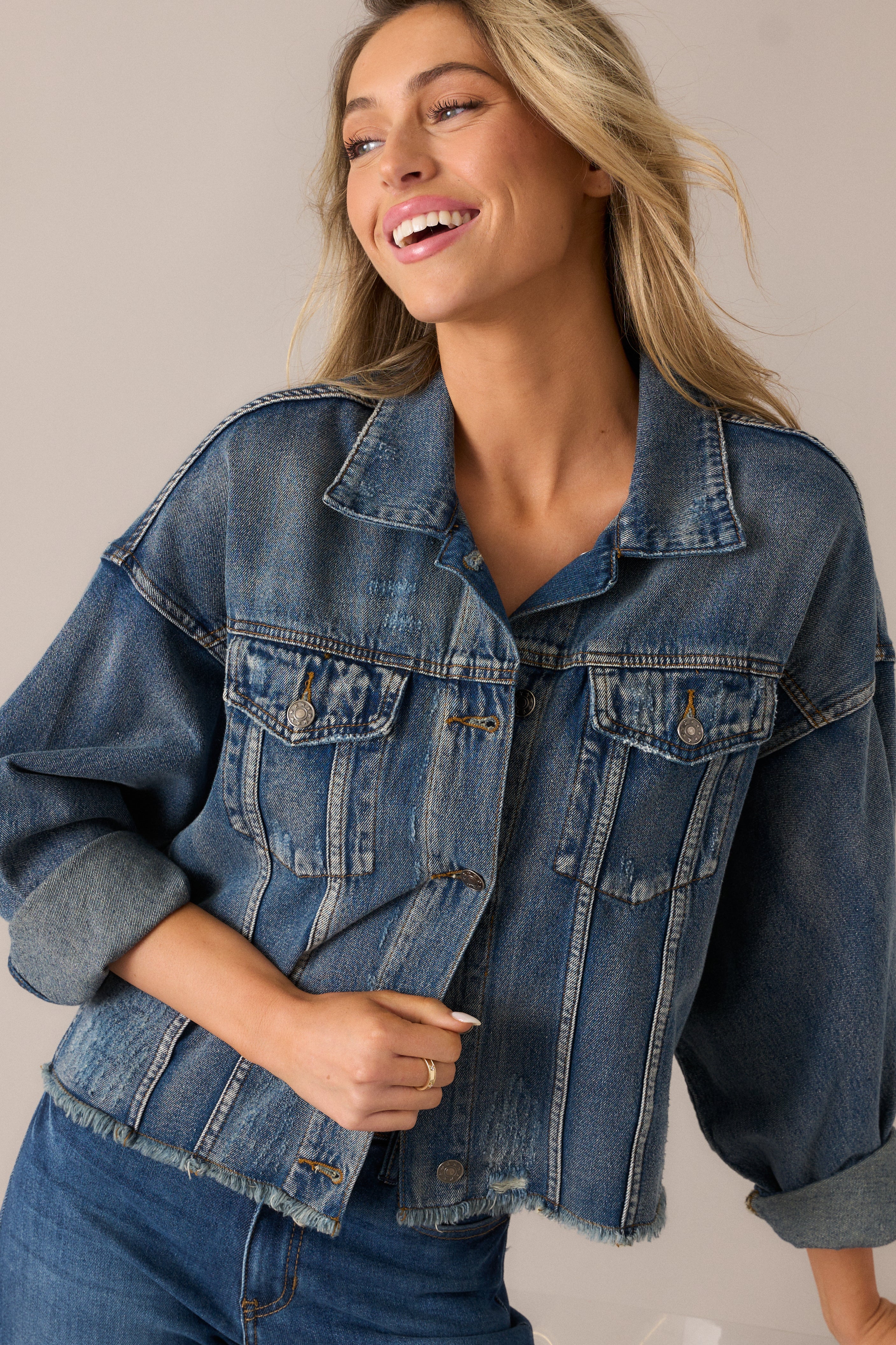 Close view of the denim jacket's chest pockets and textured distressed finish, emphasizing the folded collar and button-front design.