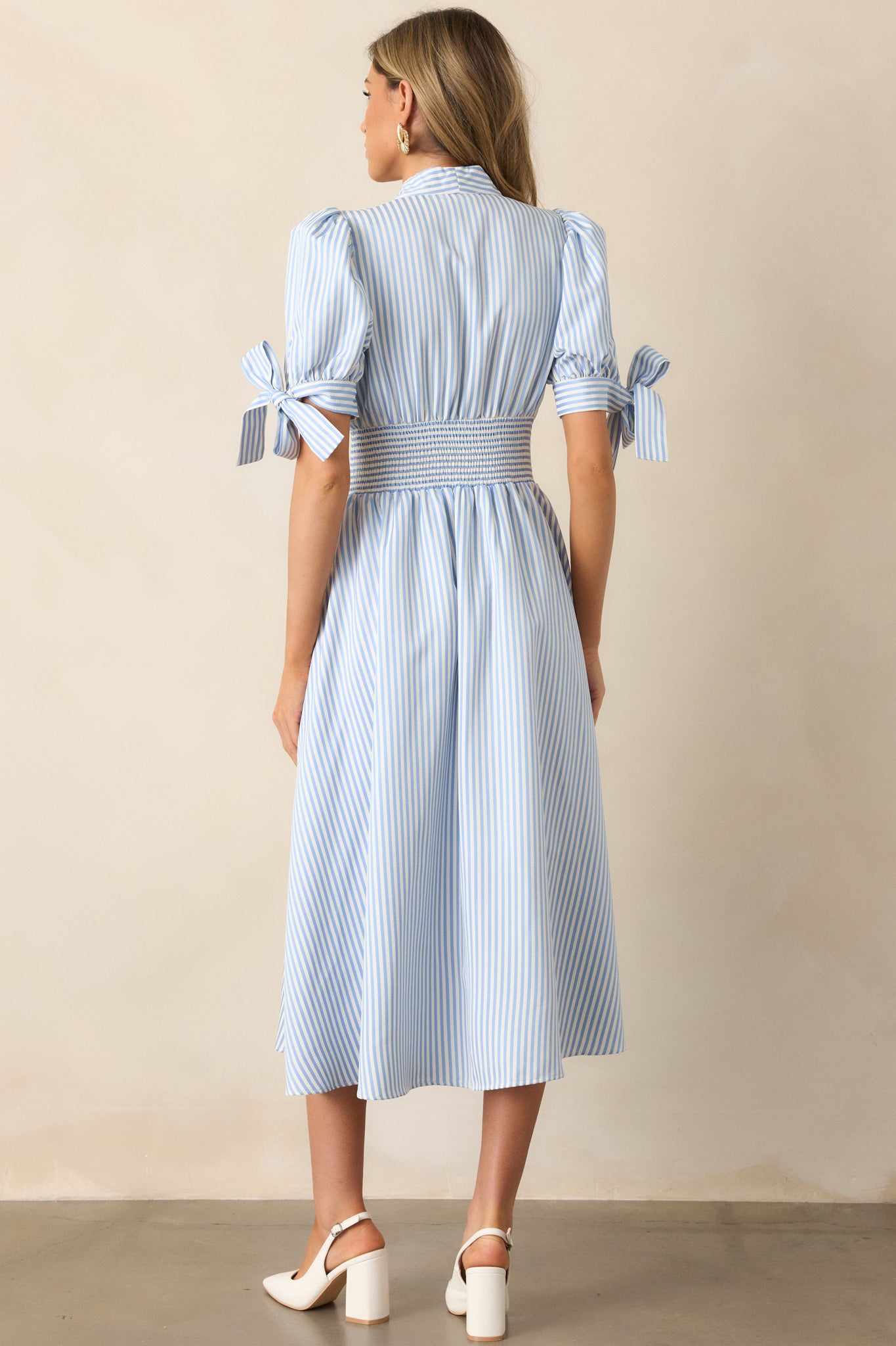  Back view of the blue stripe dress, highlighting the fitted smocked waist and flowing skirt, with a seamless stripe pattern and long sleeves.