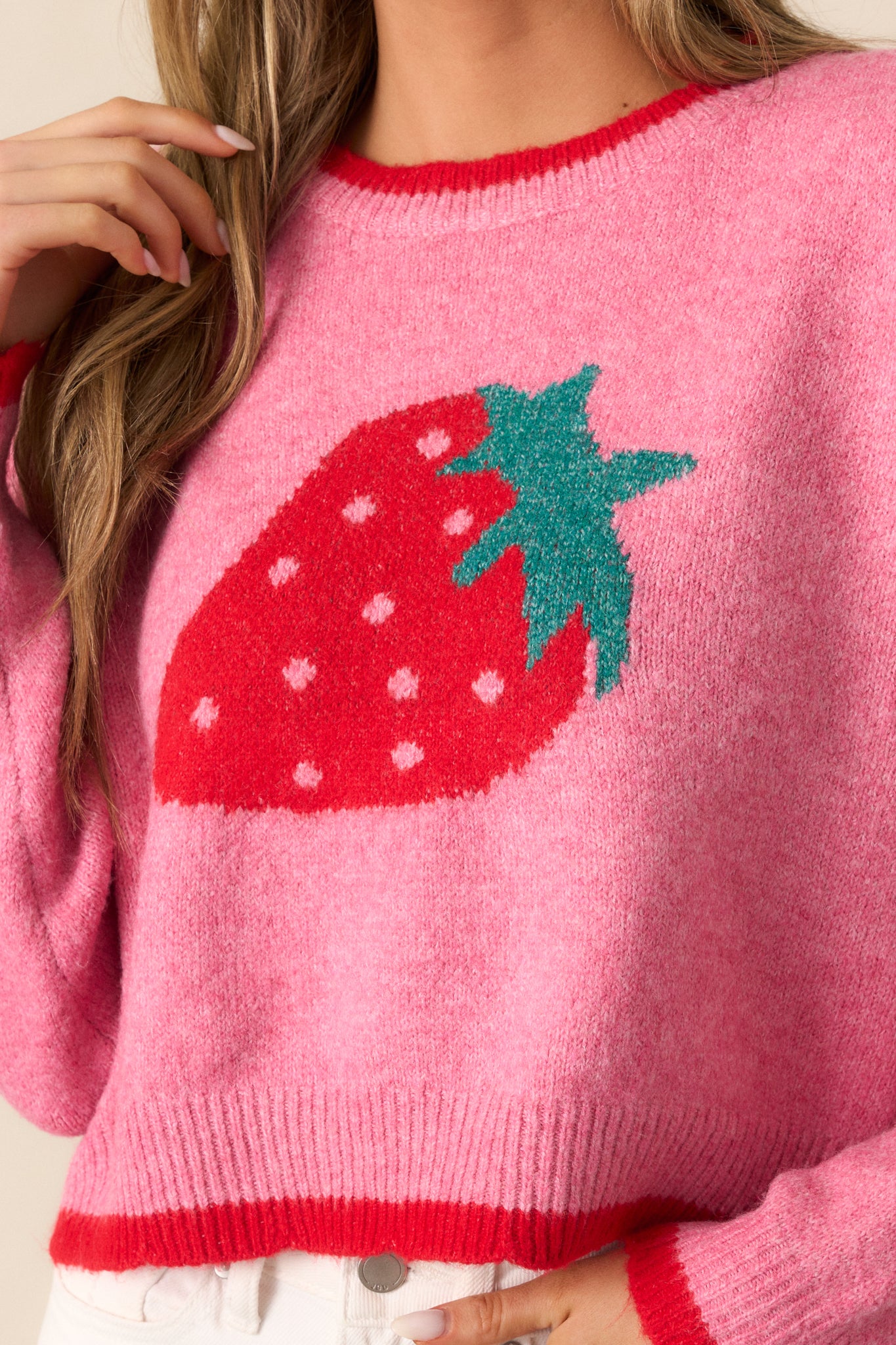 A lively zoom-in on the juicy strawberry design and soft, textured knit of this pink sweater.