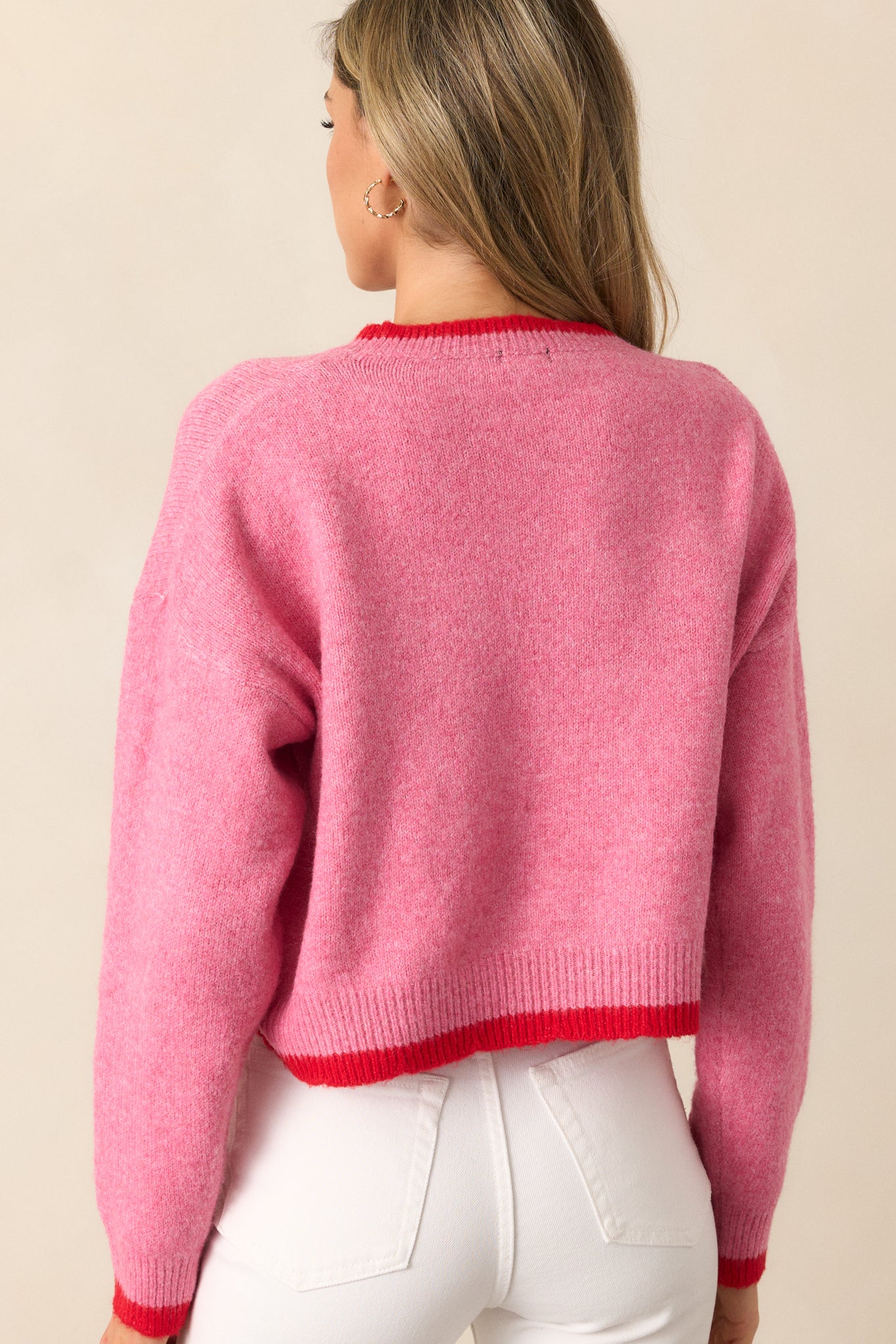 The back view of a pink sweater, featuring bold strawberries, bright red trim, and cozy long sleeves.