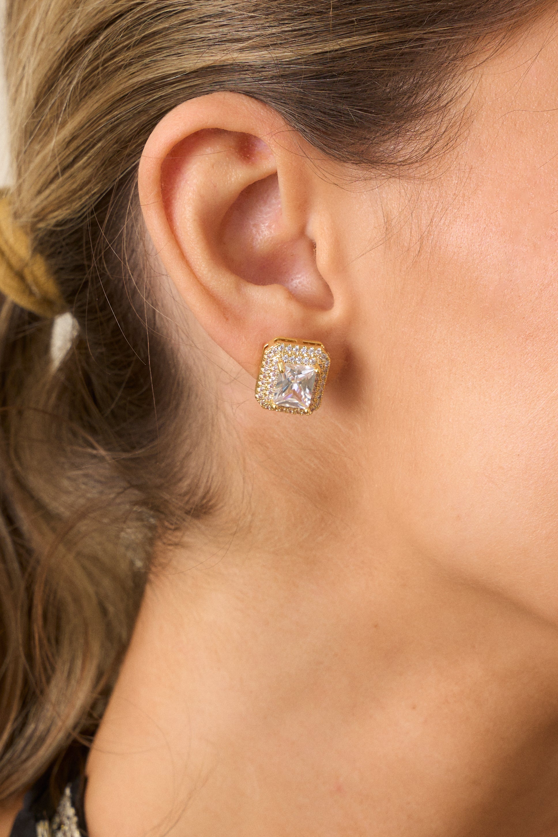 A detailed close-up of the gold earrings highlighting the large center rhinestone, tiny surrounding rhinestones, and gold hardware.