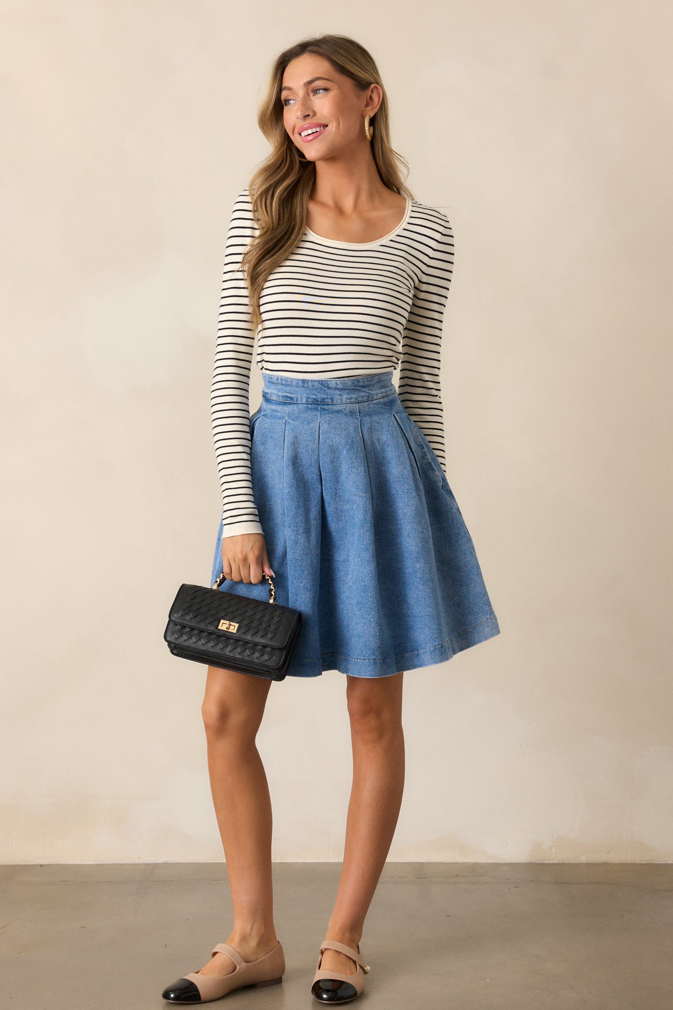 A front-facing view of a high-waisted denim skirt featuring functional hip pockets and subtle pleats.