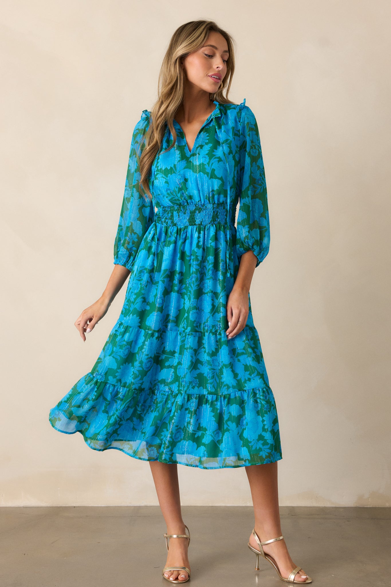 A full-length display of the blue dress, highlighting the smocked waistband, v-neckline with self-tie collar, and 3/4 sleeves with ruffle details.