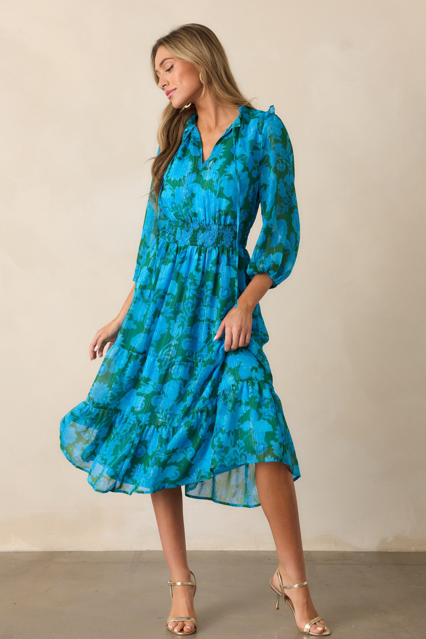 The blue dress shown in a full view, emphasizing the v-neckline, smocked waistband, and midi length with a tiered hem.