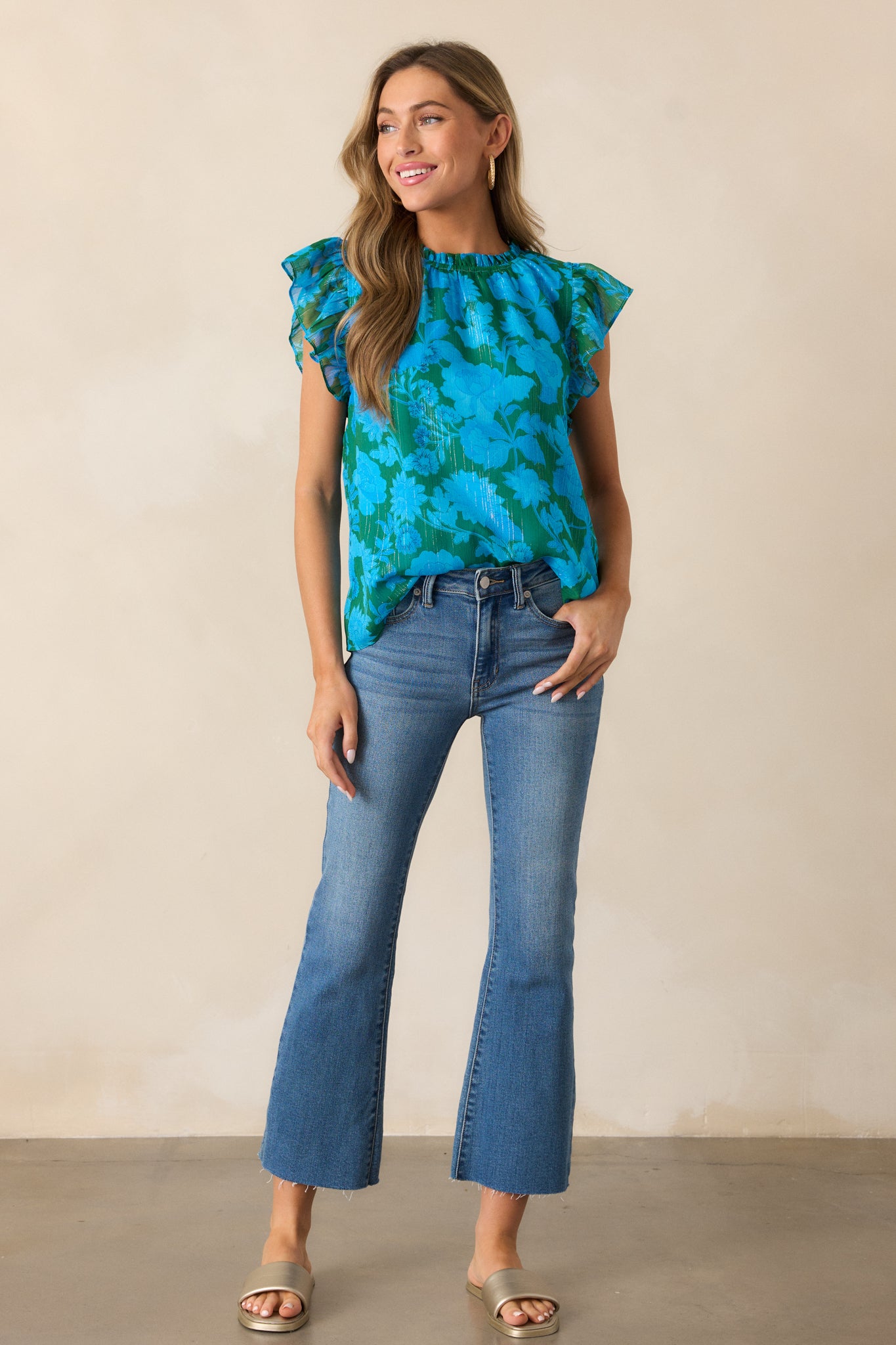 A full view of the blue blouse, highlighting the high ruffle detailing, short flutter sleeves, and beautiful floral print.