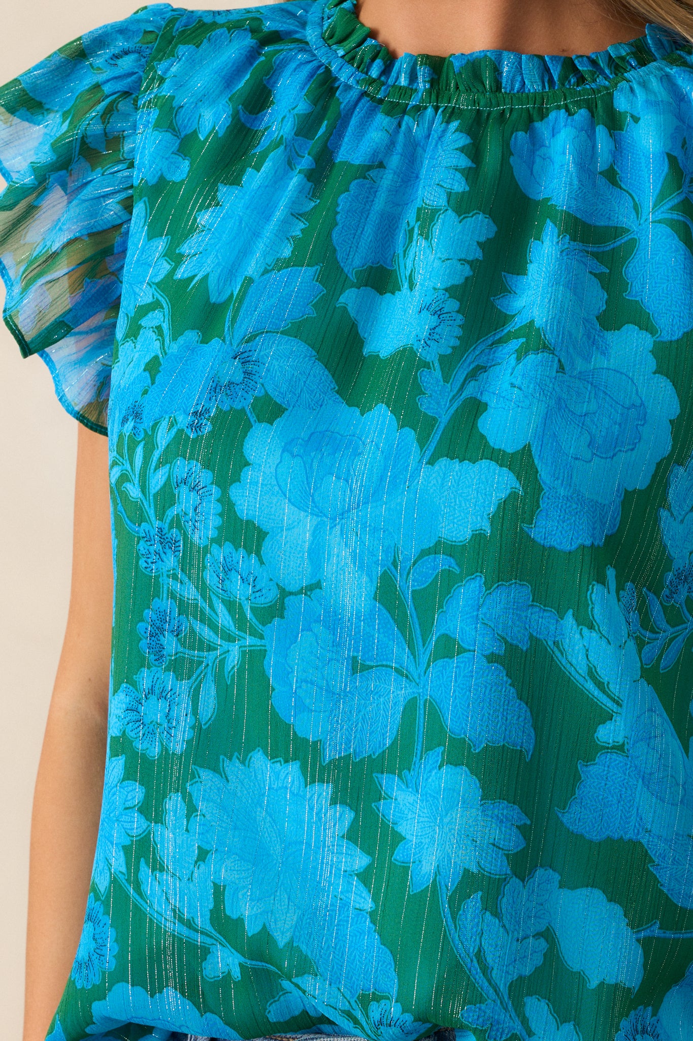 An up-close detail shot of the floral print and high ruffle detailing on the blue blouse.