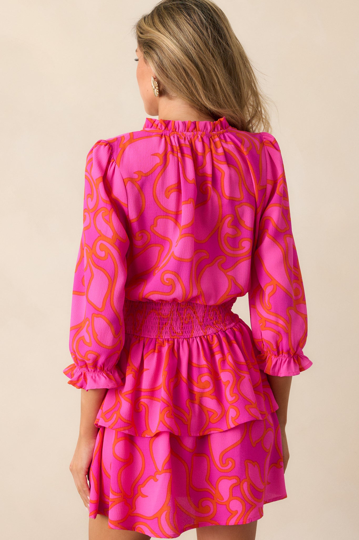 A view of the back of the magenta mini dress, highlighting the flow of the tiered skirt and the continuation of the beautiful orange floral pattern.