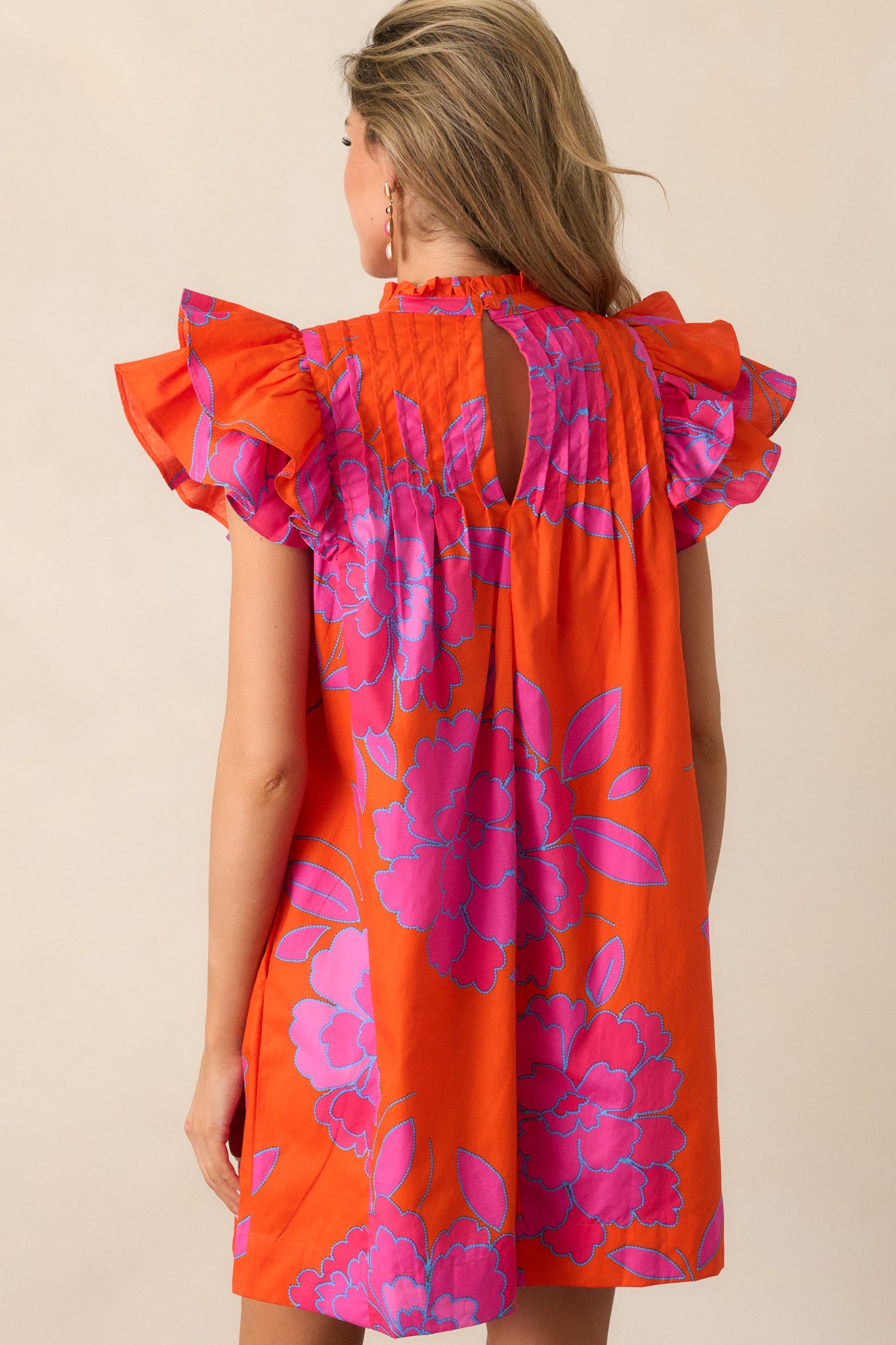 A view of the back of the orange mini dress, highlighting the single button closure and relaxed fit of the fabric.