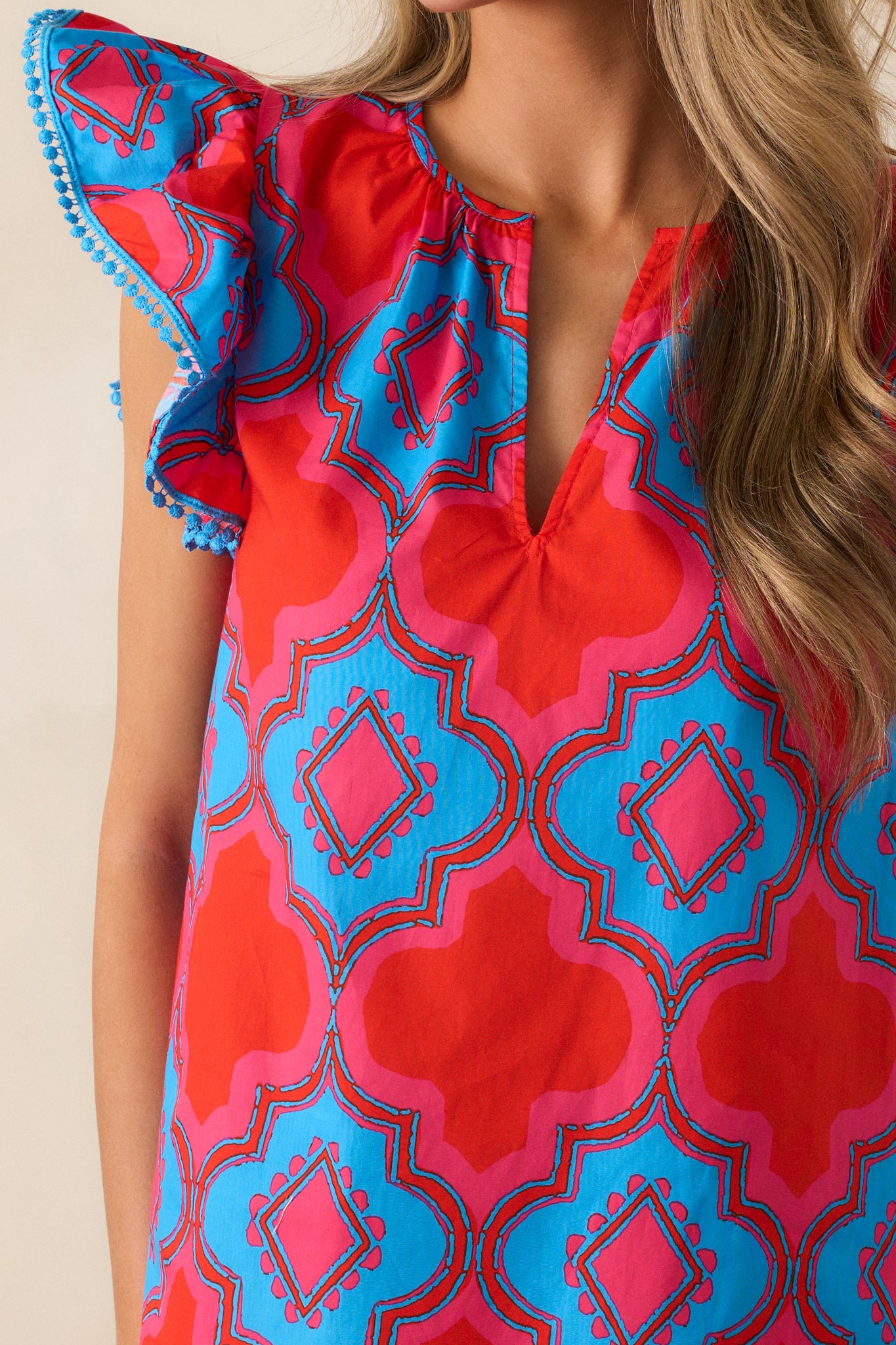 Close-up of the blue embroidered trim on the short flutter sleeves of the red top, highlighting the intricate stitching and the soft flow of the fabric