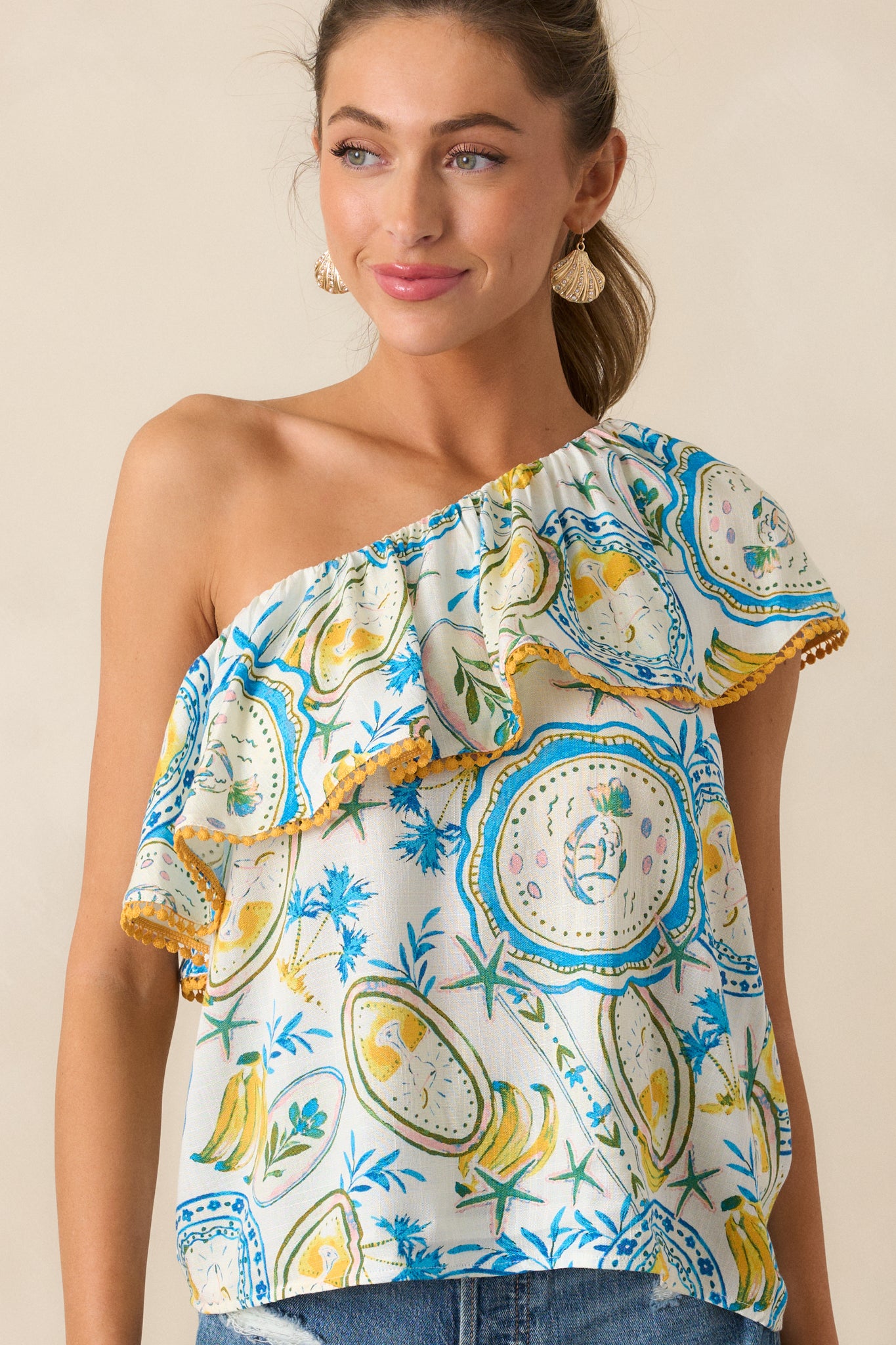 Closer view of the one-shoulder design and ruffle detailing with yellow trim on the ivory top.