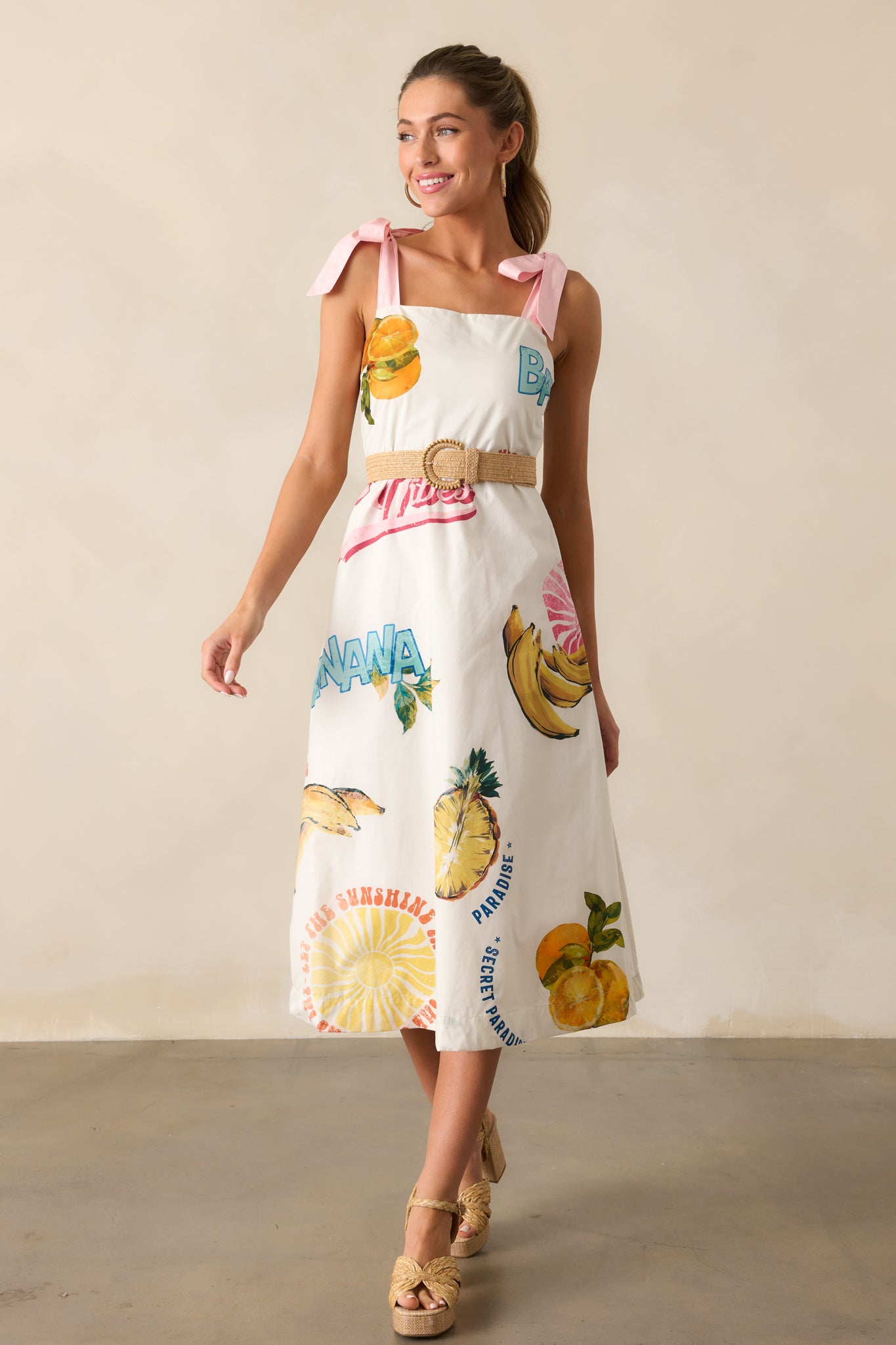 The dress in a full-length shot, featuring a beautiful tropical fruit print, smocked back detailing, and midi length.