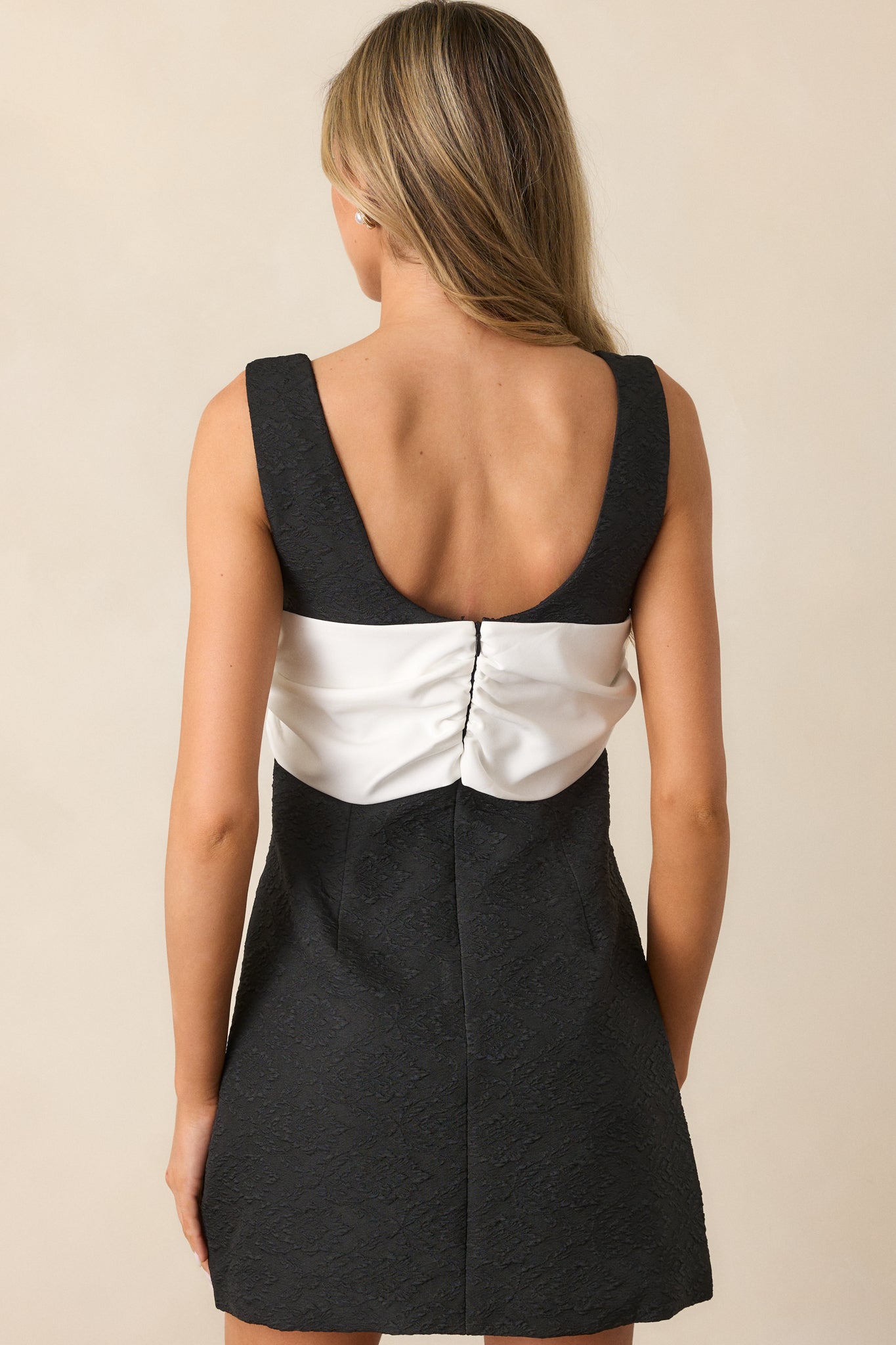 A back view of the black mini dress, featuring the discrete back zipper and the clean lines of the wide shoulder straps, flowing into the flared skirt