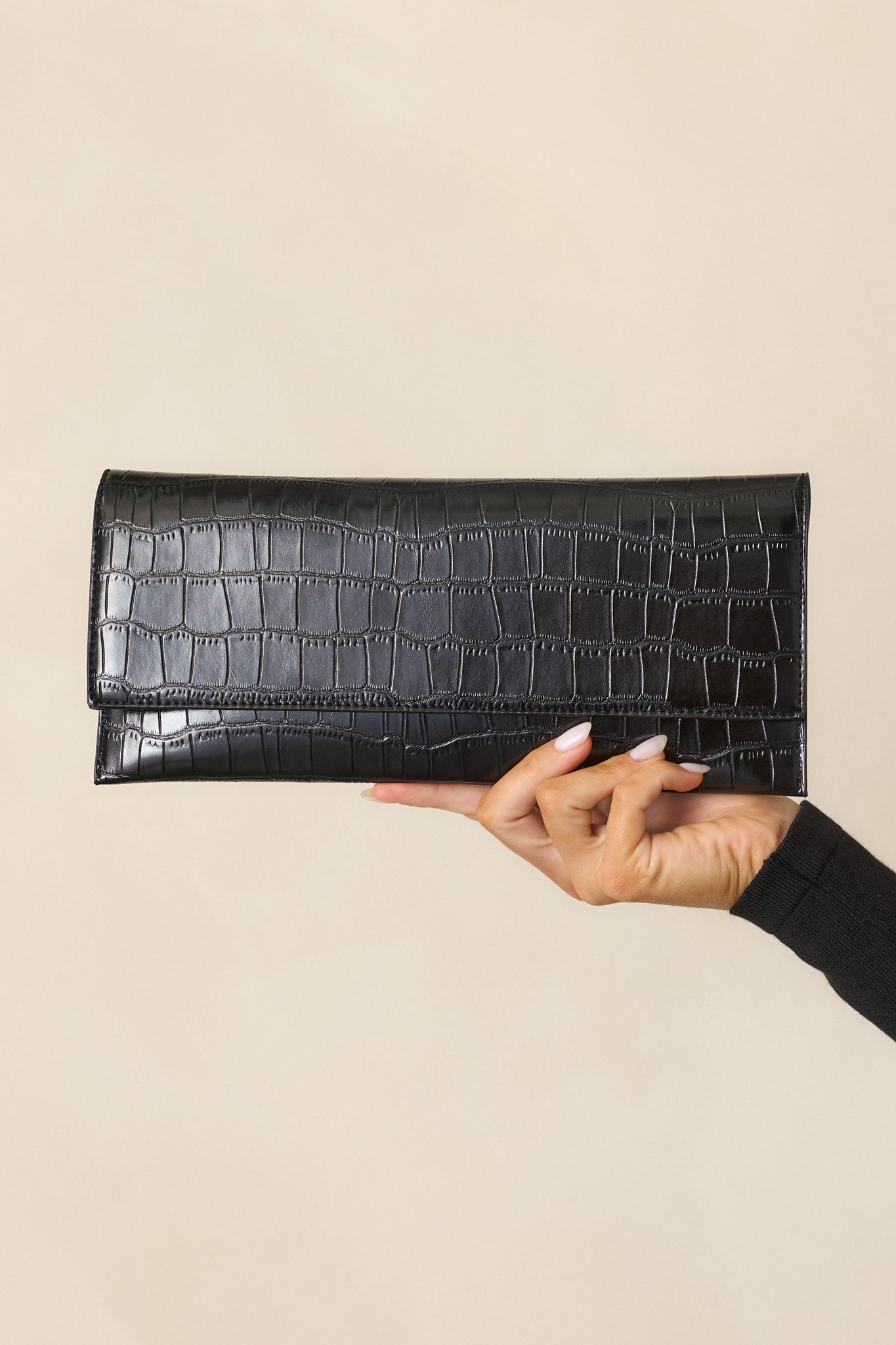 A black clutch with a textured faux leather finish and a zippered inside pouch under the magnetic closure.