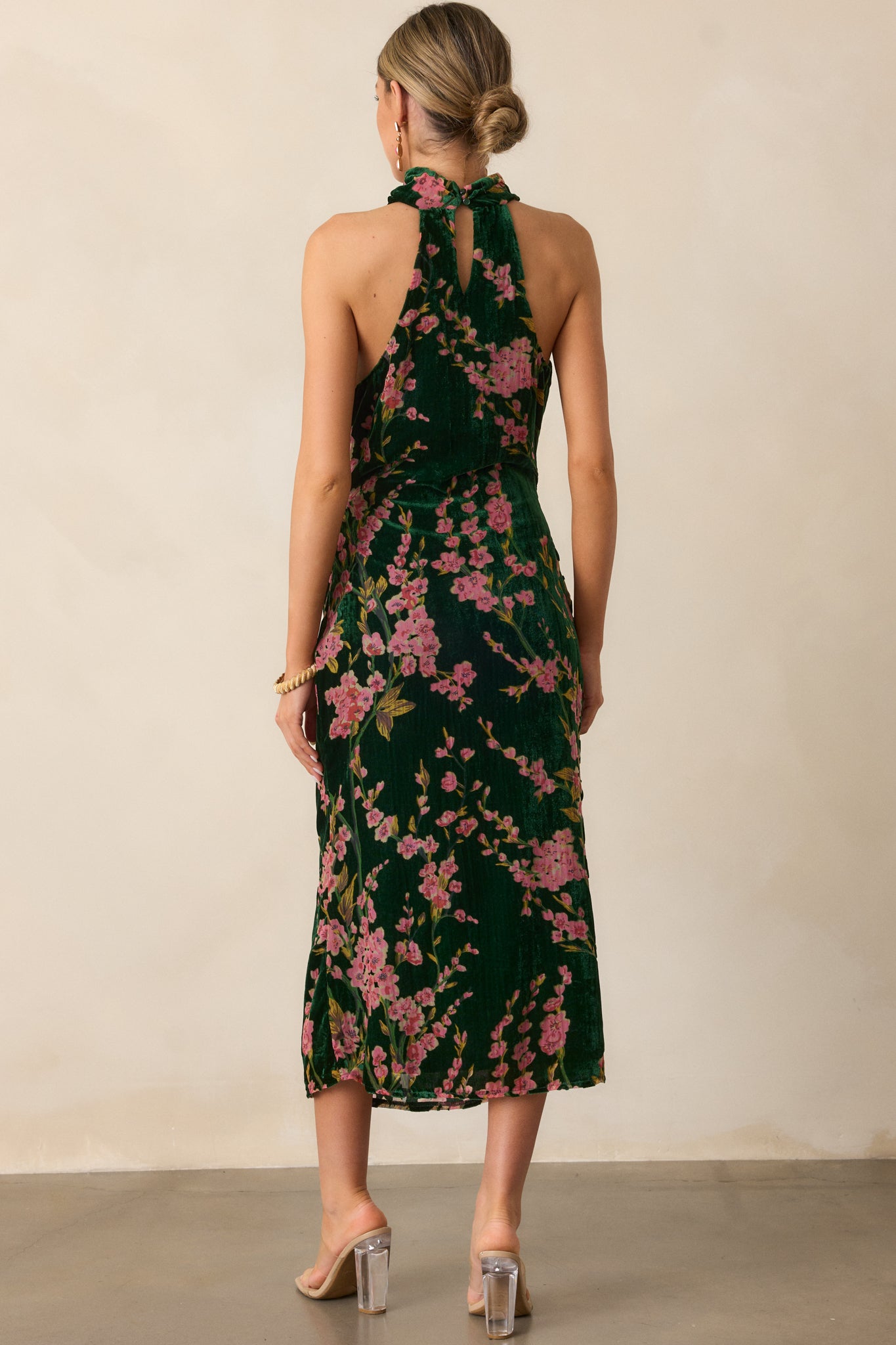 A back view of the green dress, highlighting the buttoned halter back, the discrete back zipper, and the way the velvet fabric drapes down the maxi-length skirt.