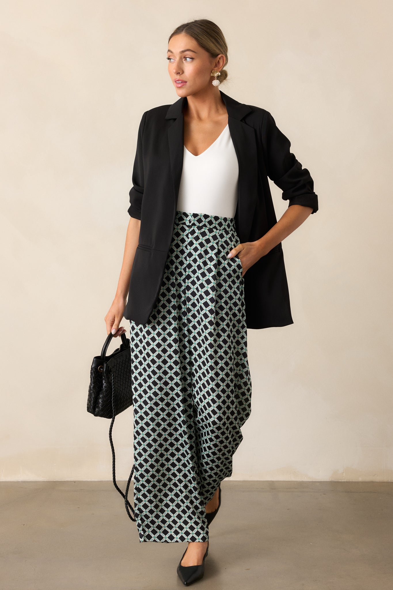 Full-length view of a black blazer with a collared neckline, padded shoulders, long sleeves, functional pockets, and a sleek tapered fit.