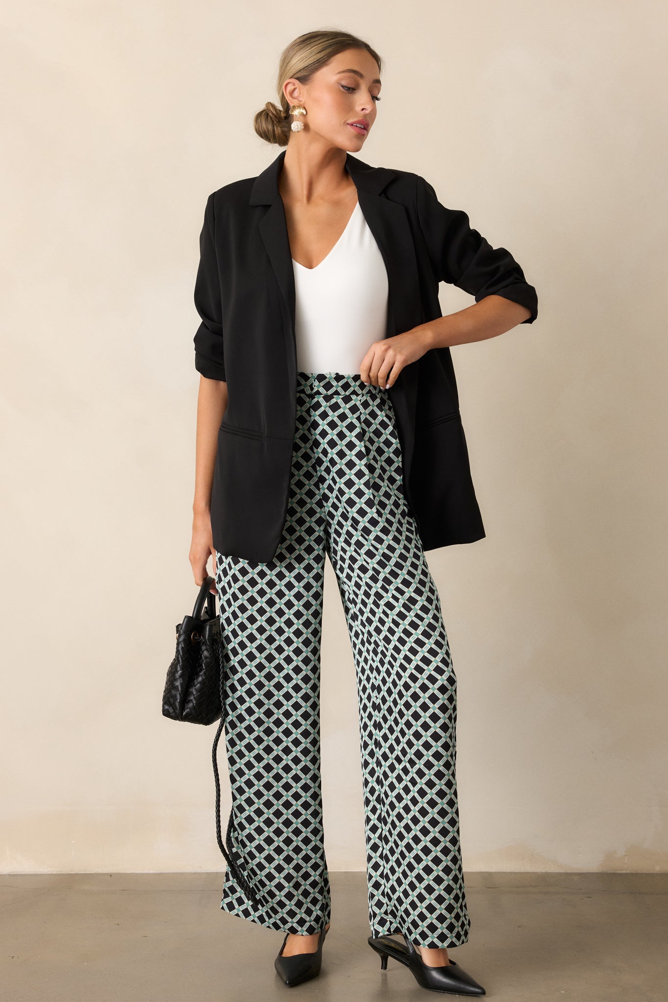 Full-length view of black pants featuring a high waist design, green and white geometric print, wide leg cut, and functional pockets.