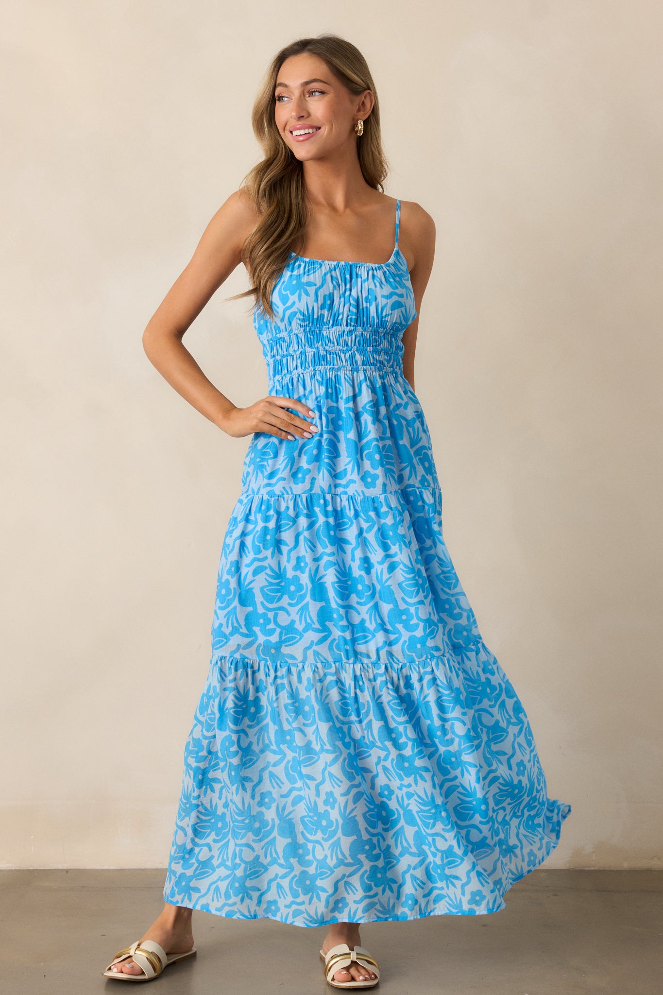 Full view of the blue maxi dress, showcasing the scoop neckline, adjustable spaghetti straps, and the flowing tiered skirt with a vibrant floral print.