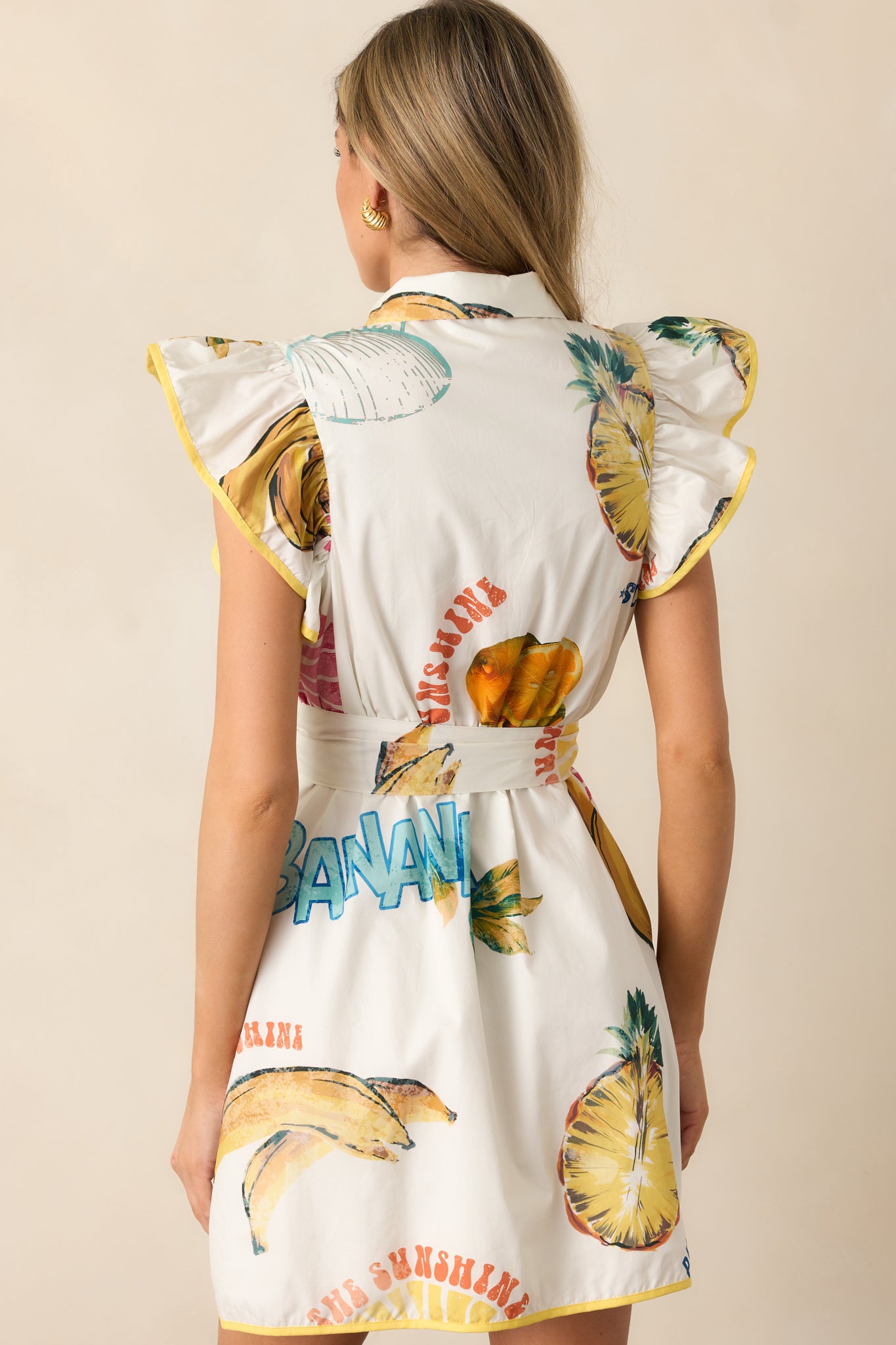 A back view of the Ivory mini dress displaying the tropical fruit pattern and the continuation of its yellow trim.