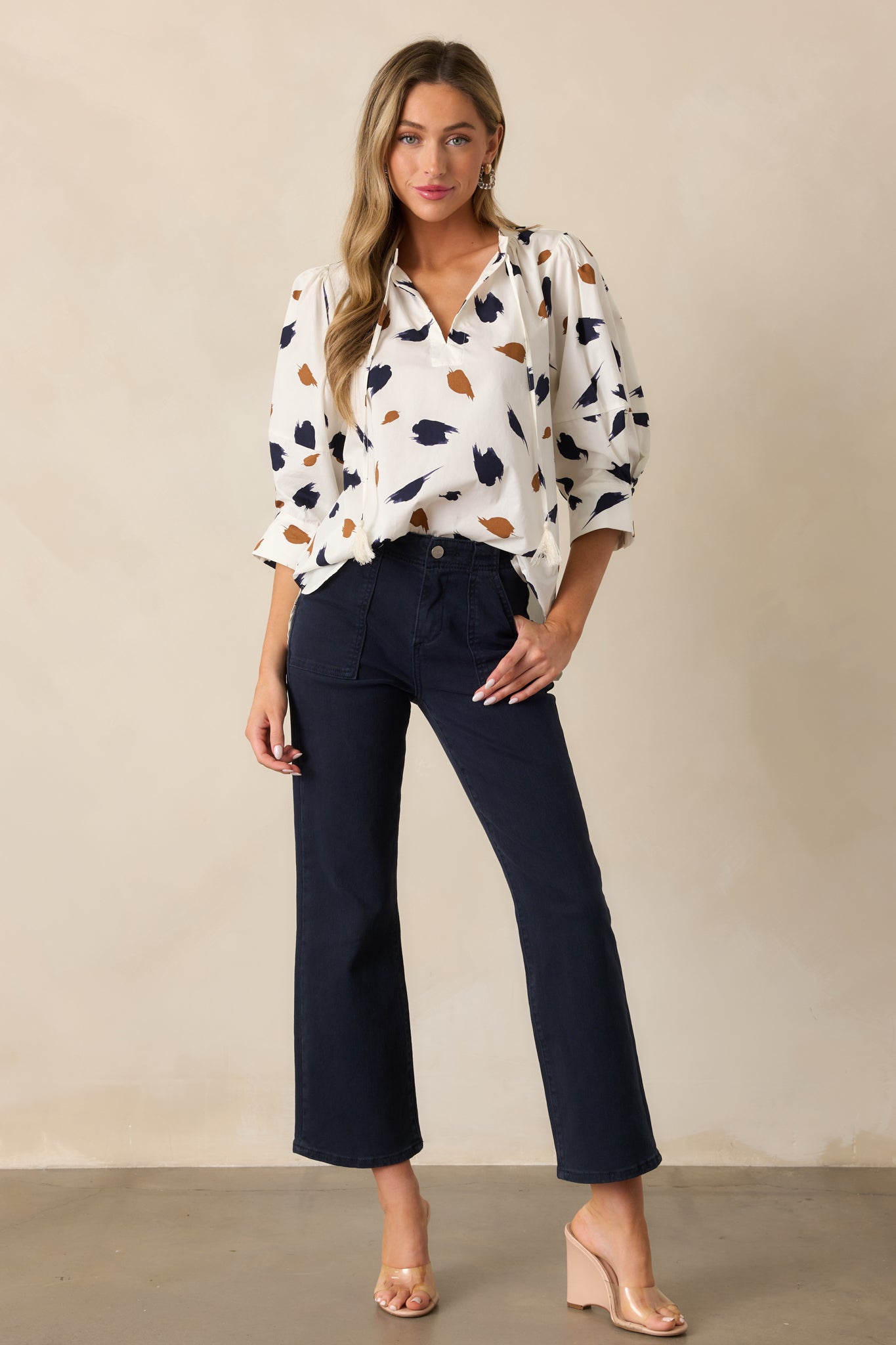 An ivory blouse featuring a v-neckline with a self-tie collar, a relaxed fit, and a brown and navy brush stroke print.

