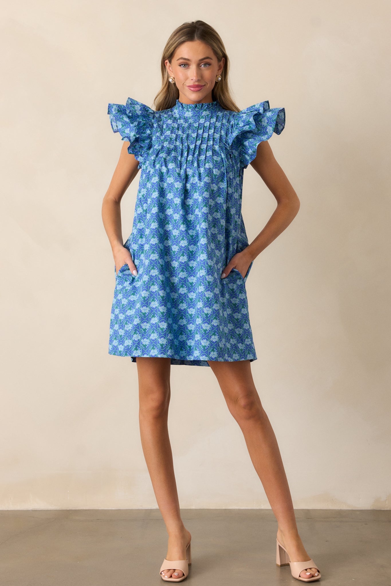 A full view of the navy mini dress showcasing its high neckline with a ruffle collar, double flutter short sleeves, and petite floral pattern.