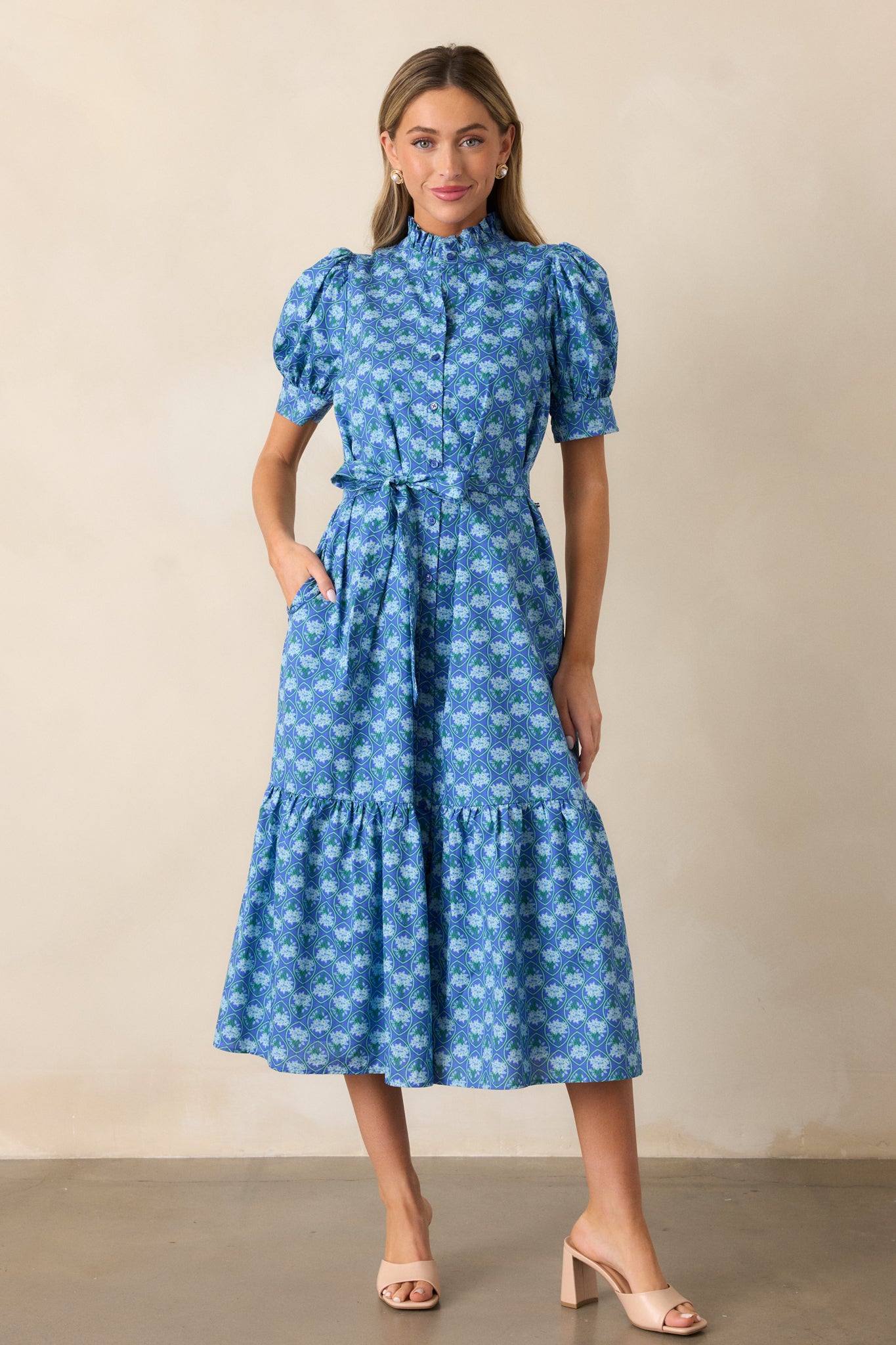 A full view of the blue dress featuring a high ruffle collar neckline, button front design, and self-tie waistband with a petite floral print.