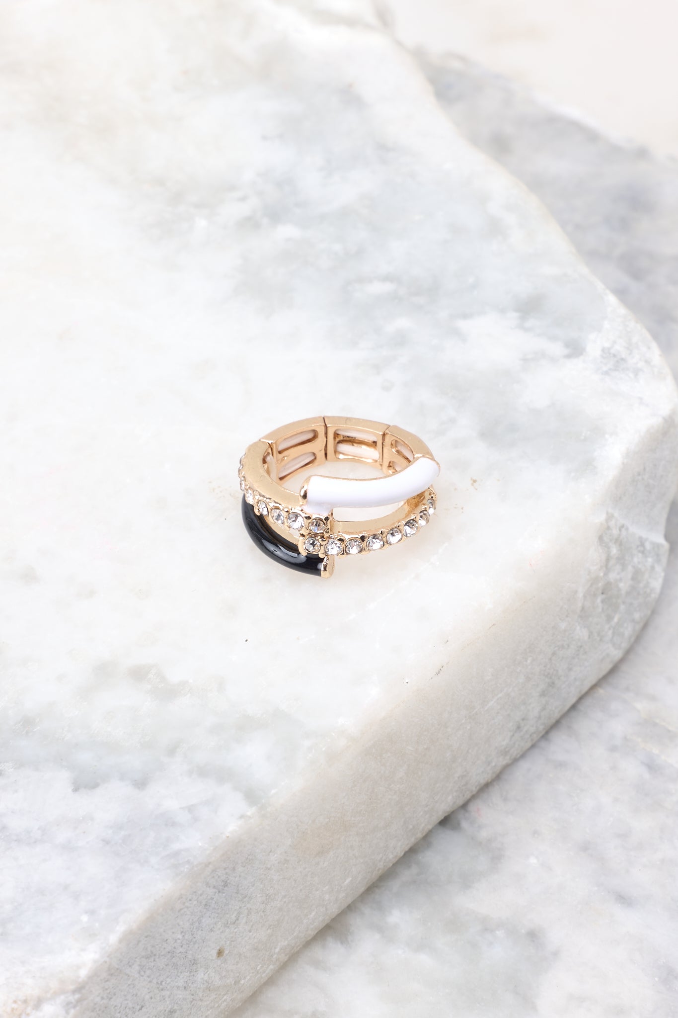 Close-up marble shot of ring that features gold hardware, black and white accents, rhinestone detailing, and elastic under the band to accommodate most ring sizes.