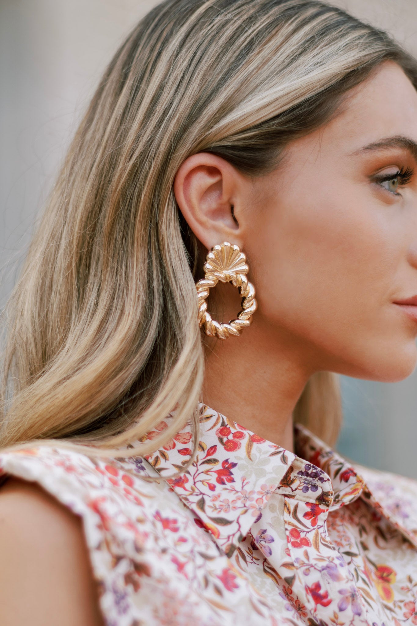 These gold earrings feature a twisted rope-like design forming an open loop, with the top part resembling a seashell, and secure post backings.