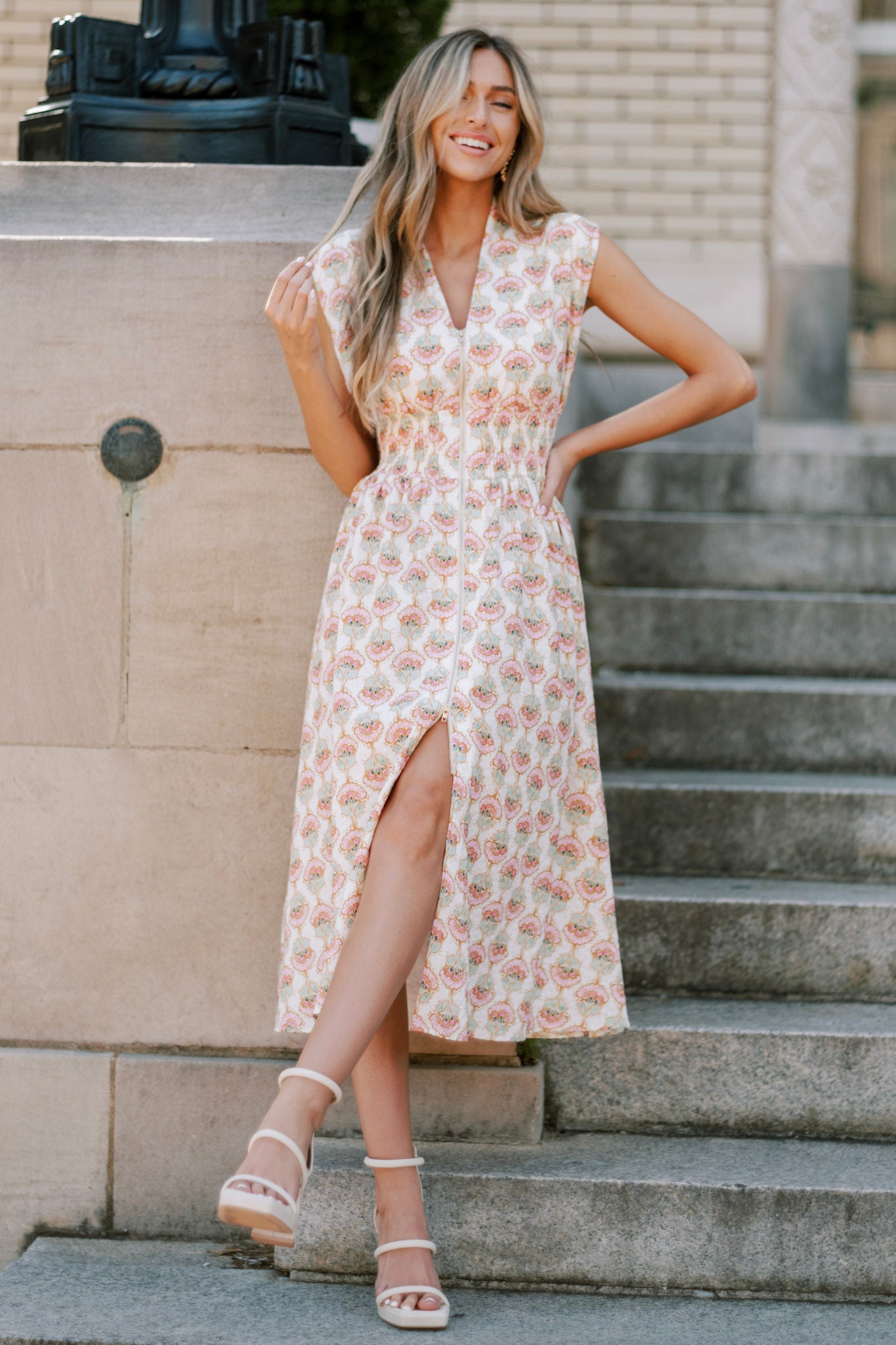 Ivory floral print dress featuring a v-neckline, wide shoulders, a full zipper front, fully smocked waist, and a front slit.