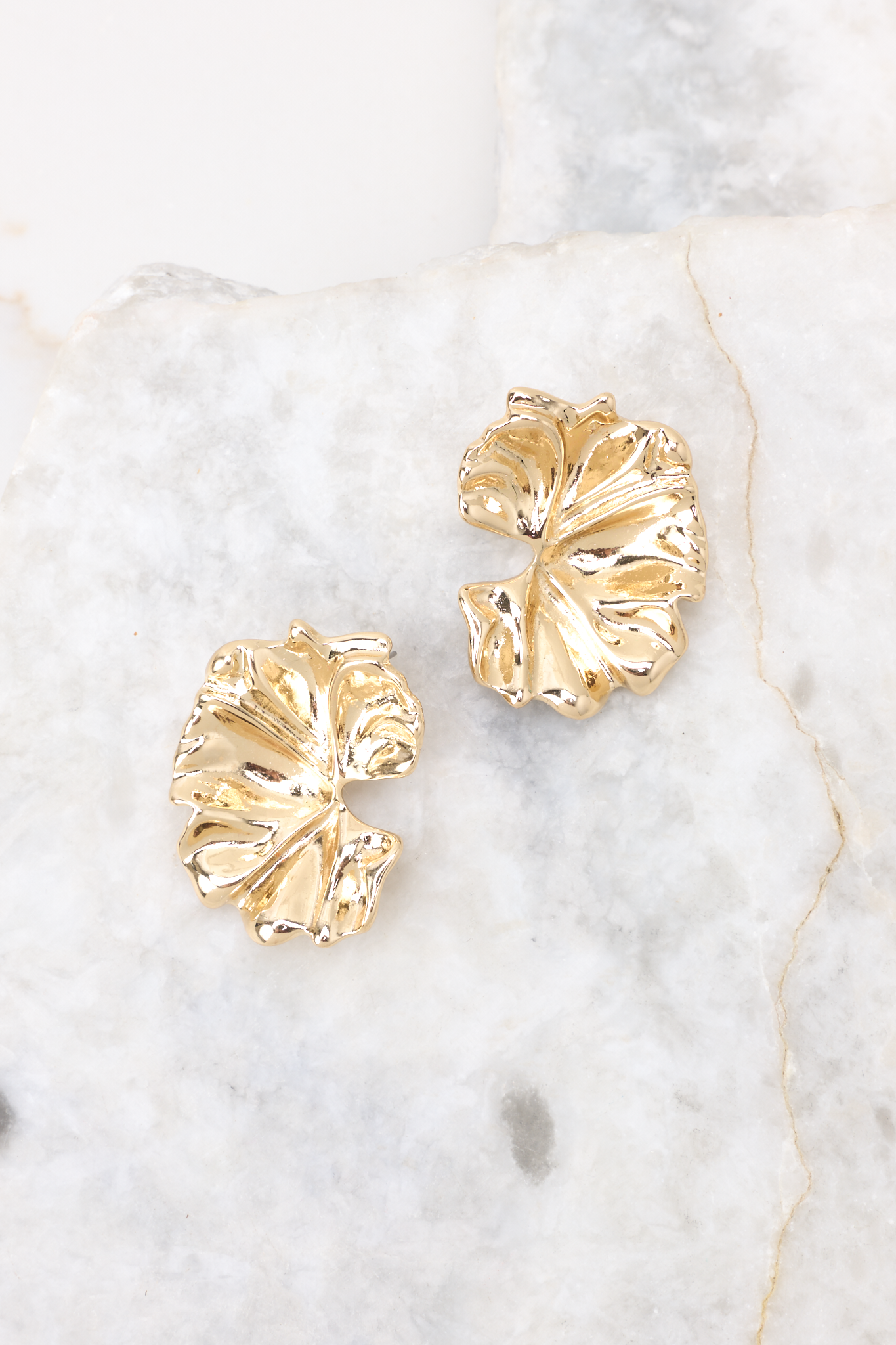 Overhead marble shot of earrings that feature gold hardware and a secure posts backing. 