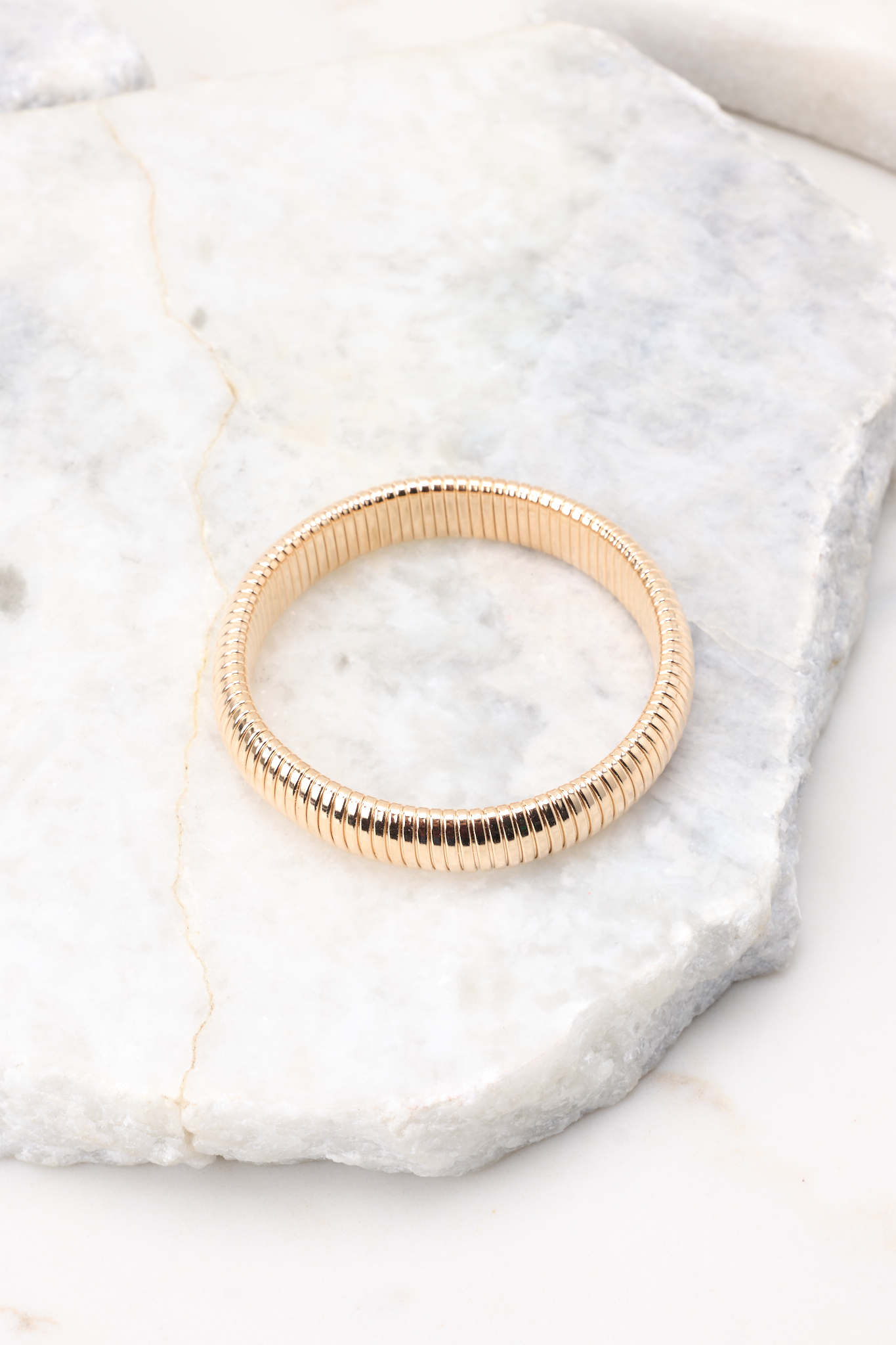 Overhead view of gold bracelet that features a circular, slip-on design with ridge detailing, and measures approximately 3" in diameter.