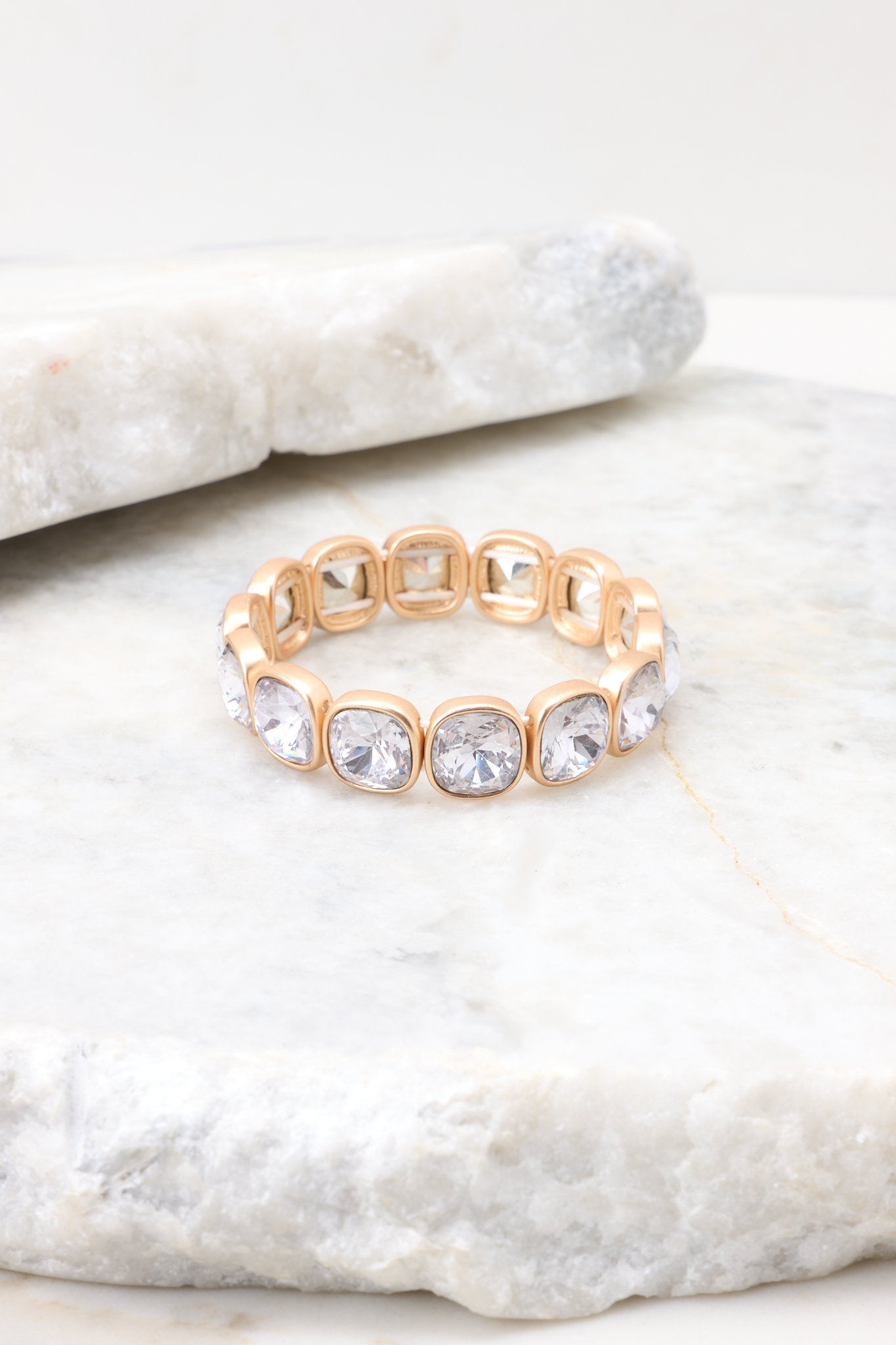 Detailed marble shot of bracelet that features gold hardware, rhinestone details, stretch band, and a slip-on style.